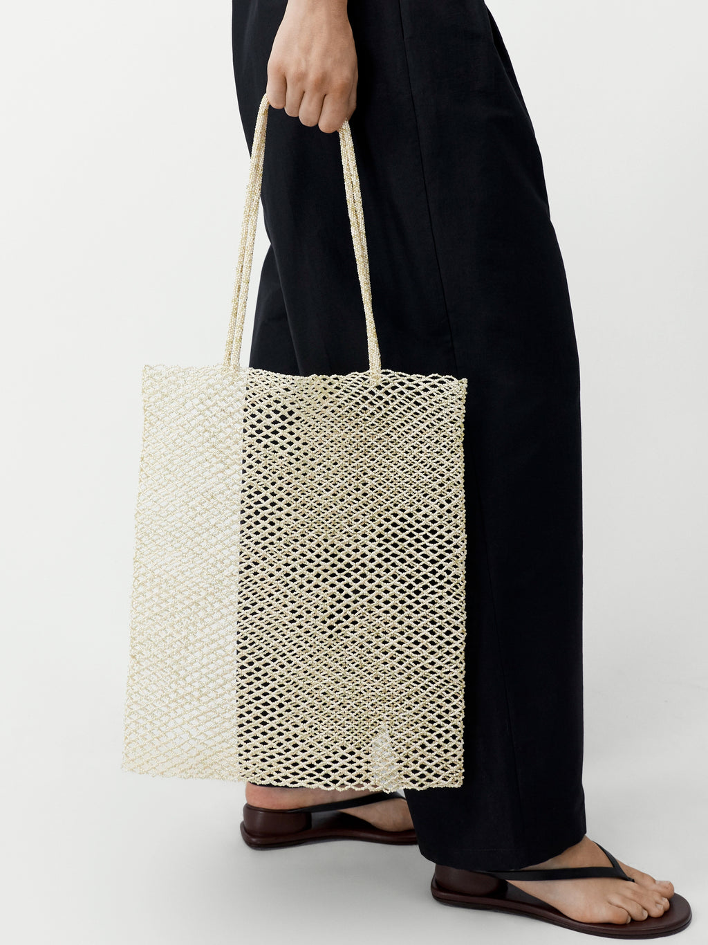 Person holding a woven beige tote bag against a white background
