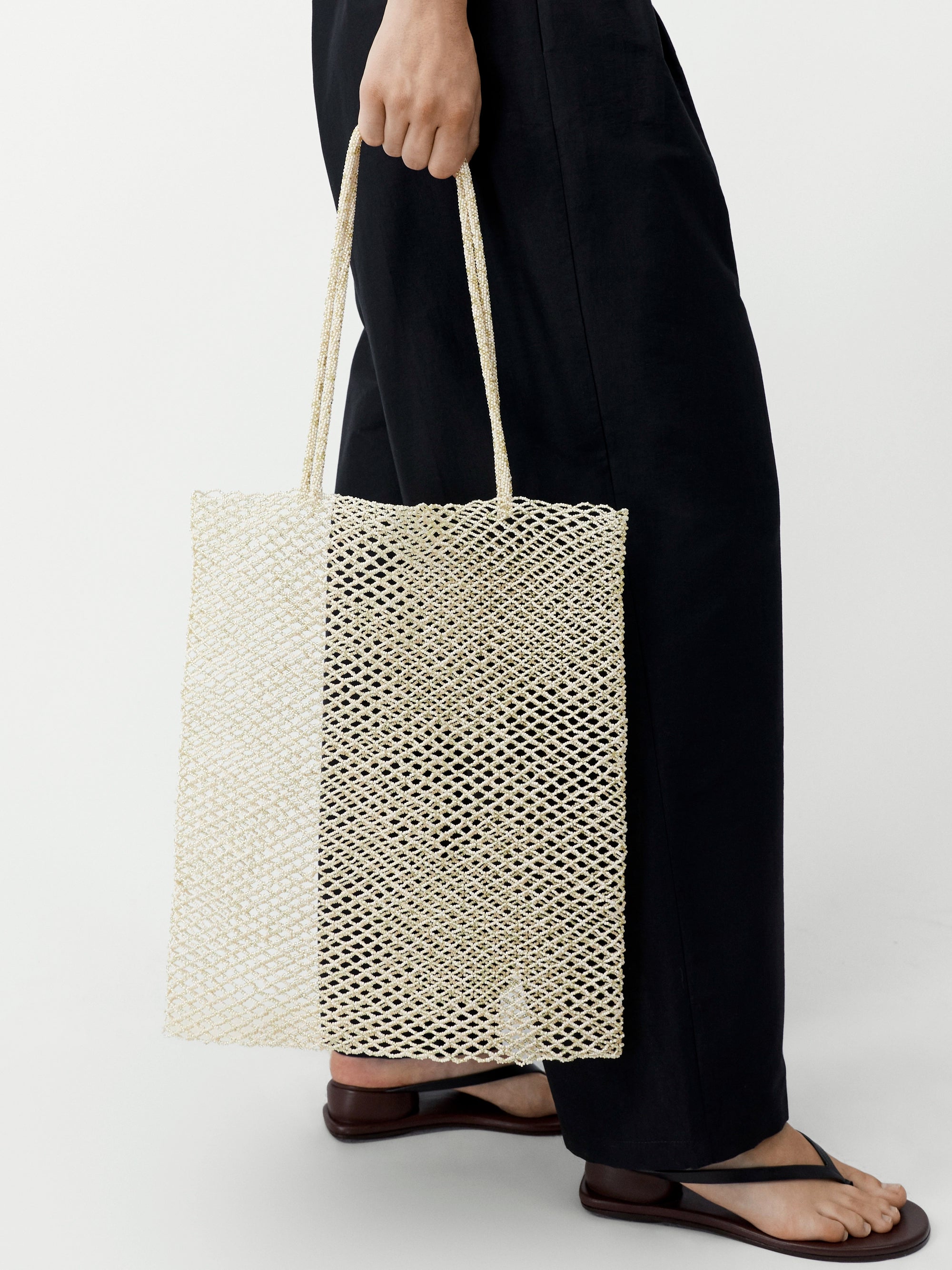Person holding a woven beige tote bag against a white background