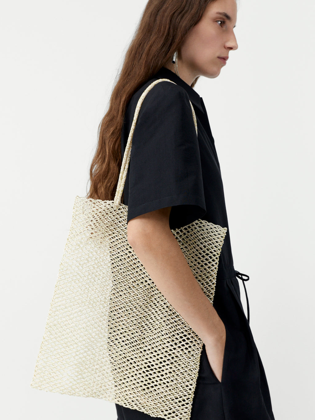 Woman carrying a beige woven bag on a plain background