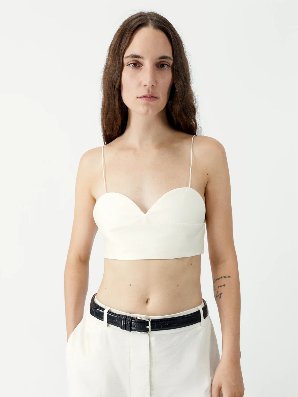 Woman wearing a white strapless top and white pants on a plain background