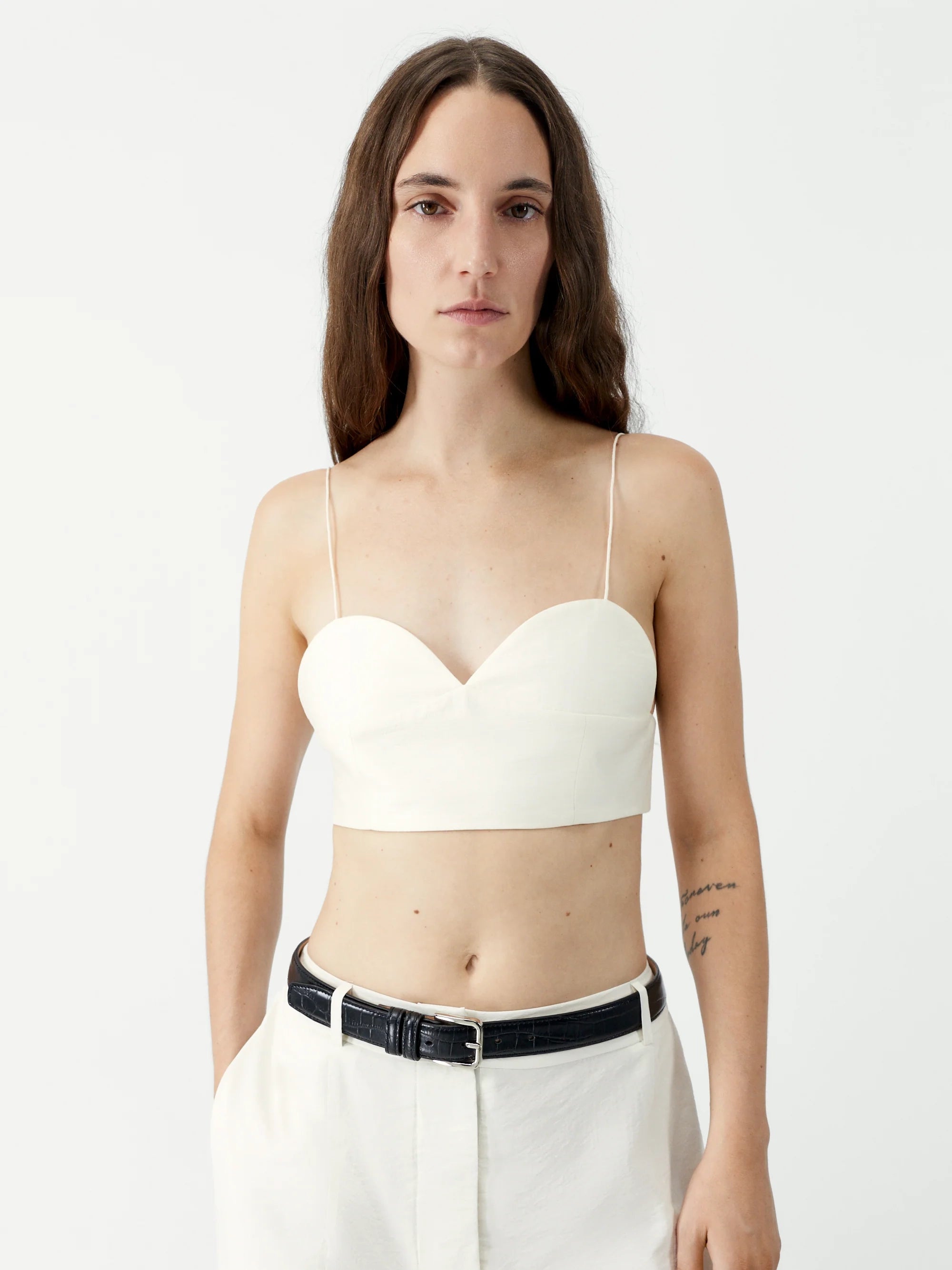 Woman wearing a white strapless top and white pants on a plain background