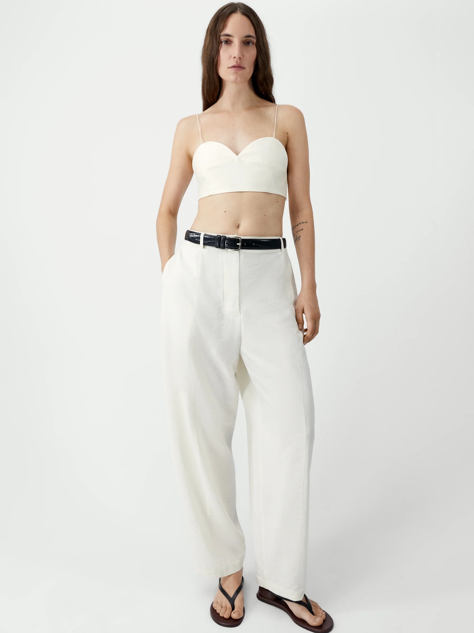 Woman wearing a white strapless top and high-waisted white pants on a white background