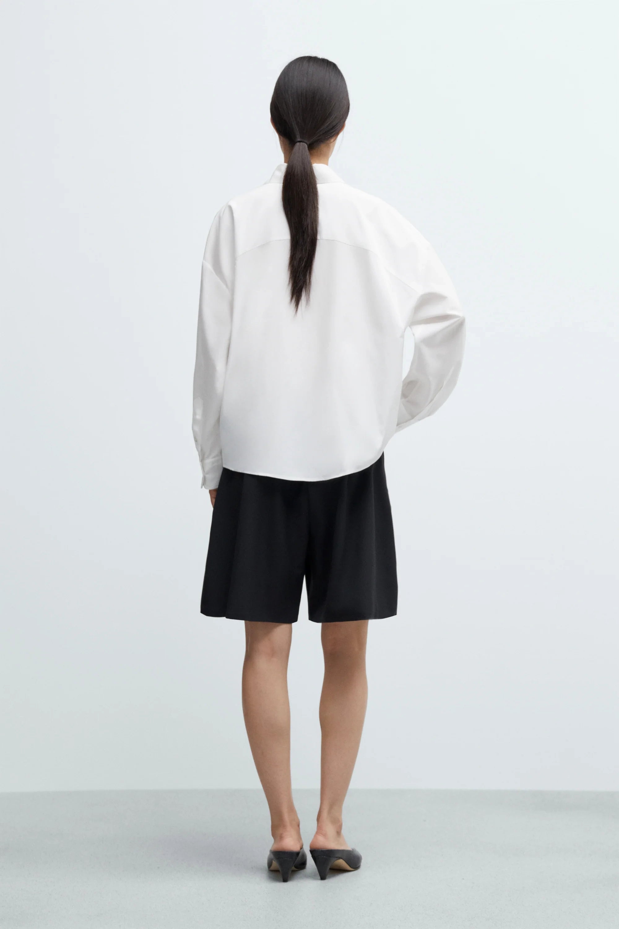 Person wearing a white shirt and black shorts on a plain background