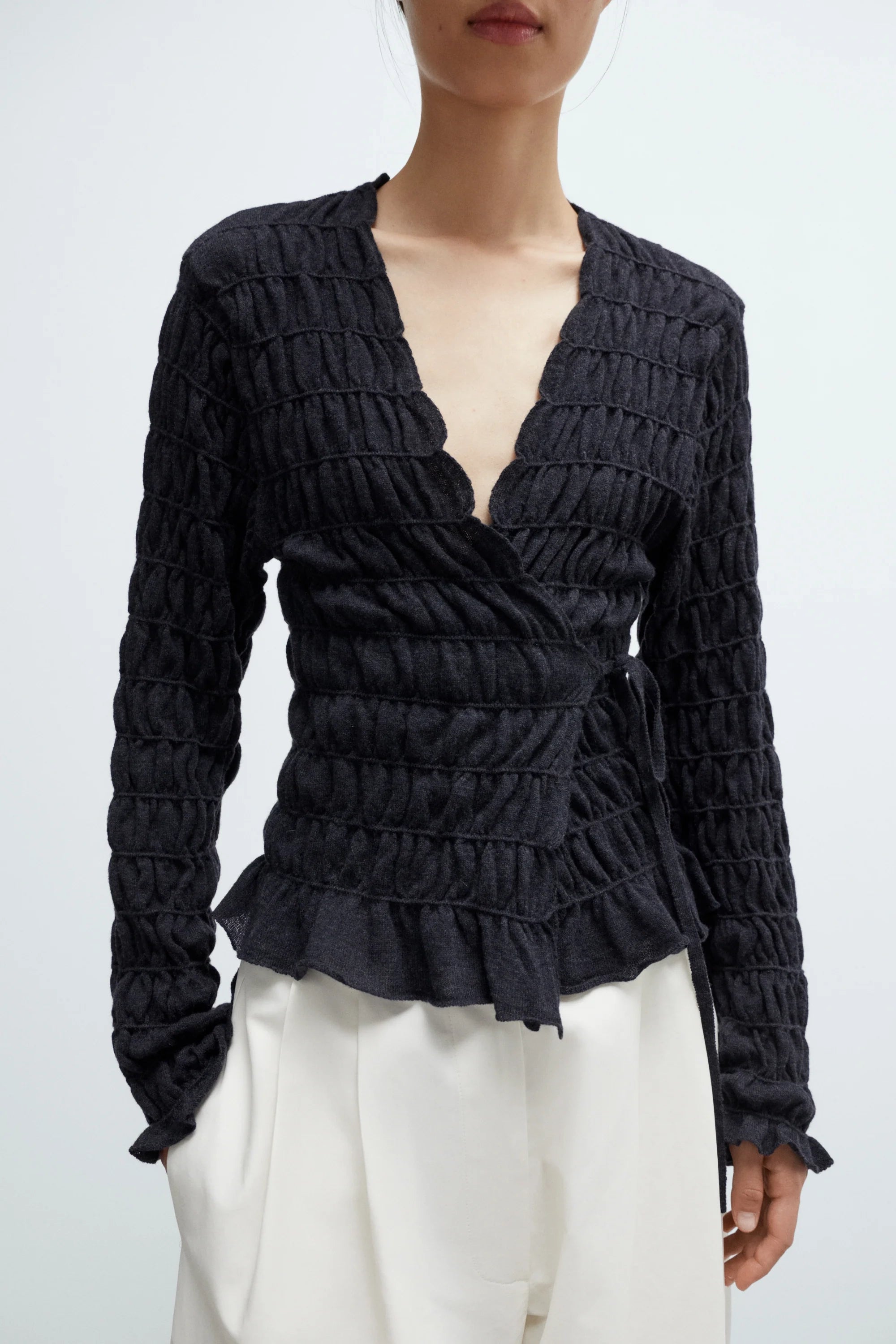 Black textured blouse with ruffled details worn by a person on a white background