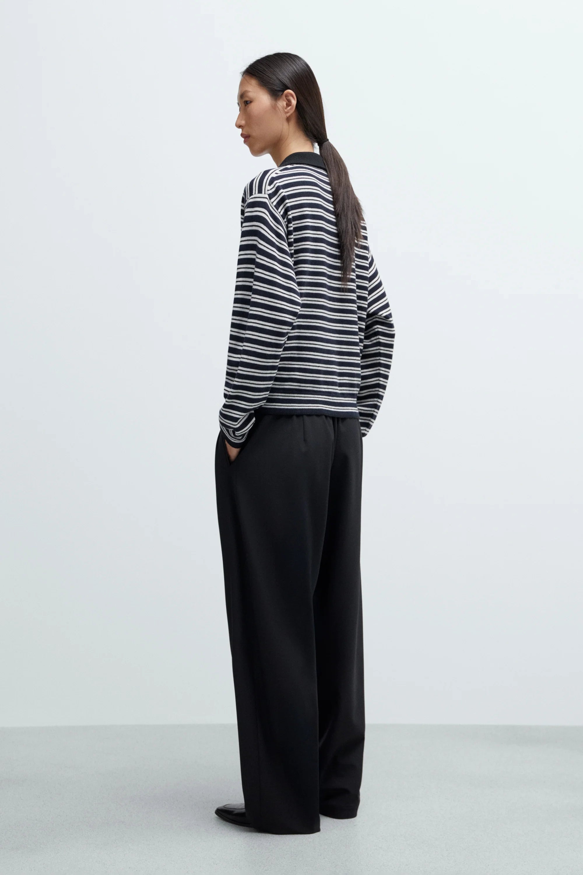 Person wearing a striped sweater and black pants on a white background