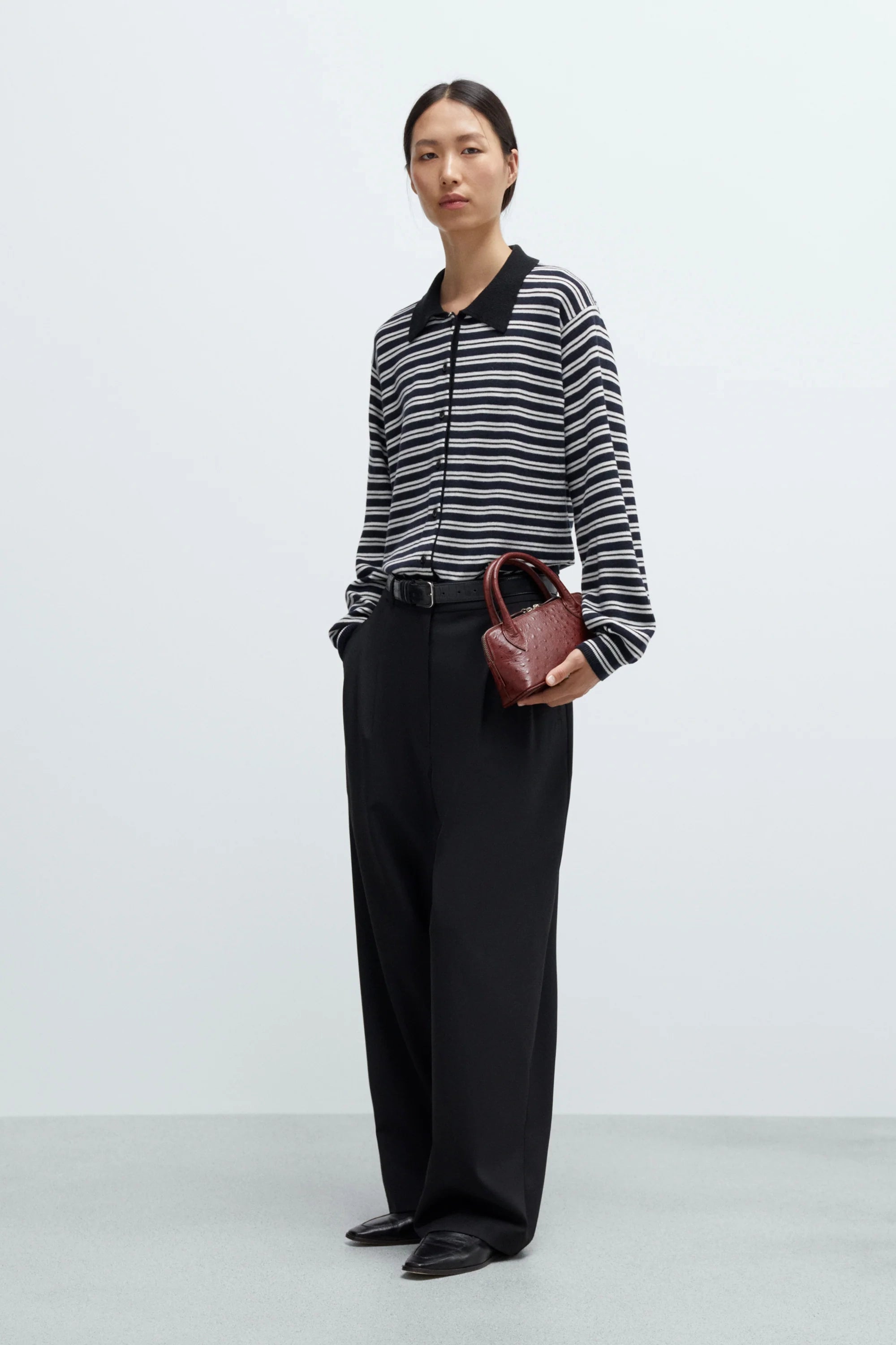Person wearing a black and white striped shirt with wide-leg pants and holding a brown handbag on a white background
