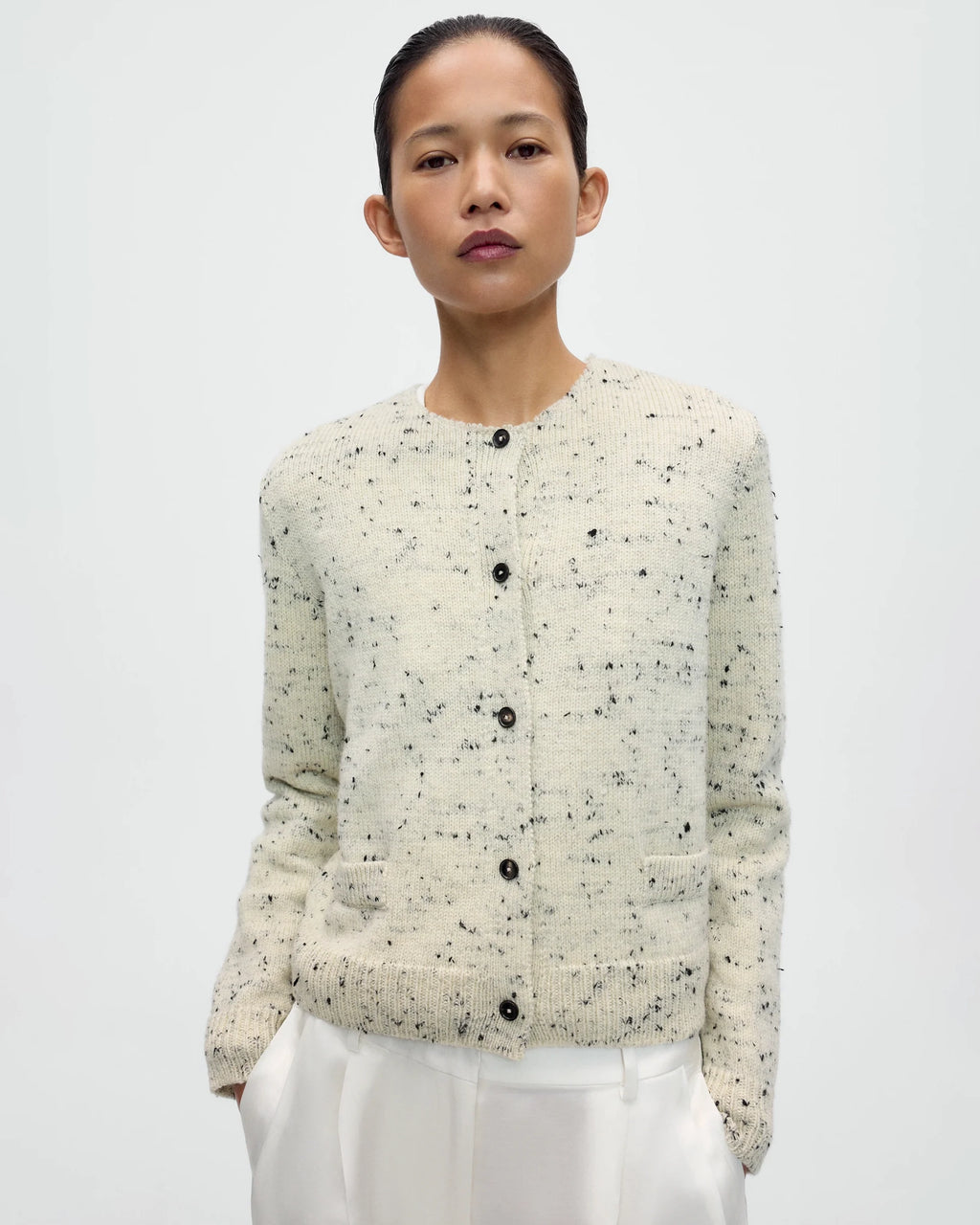 Model wearing CORDERA Merino Wool Flecked Cardigan in natural with a flecked chunky knit, button front and patch pockets.