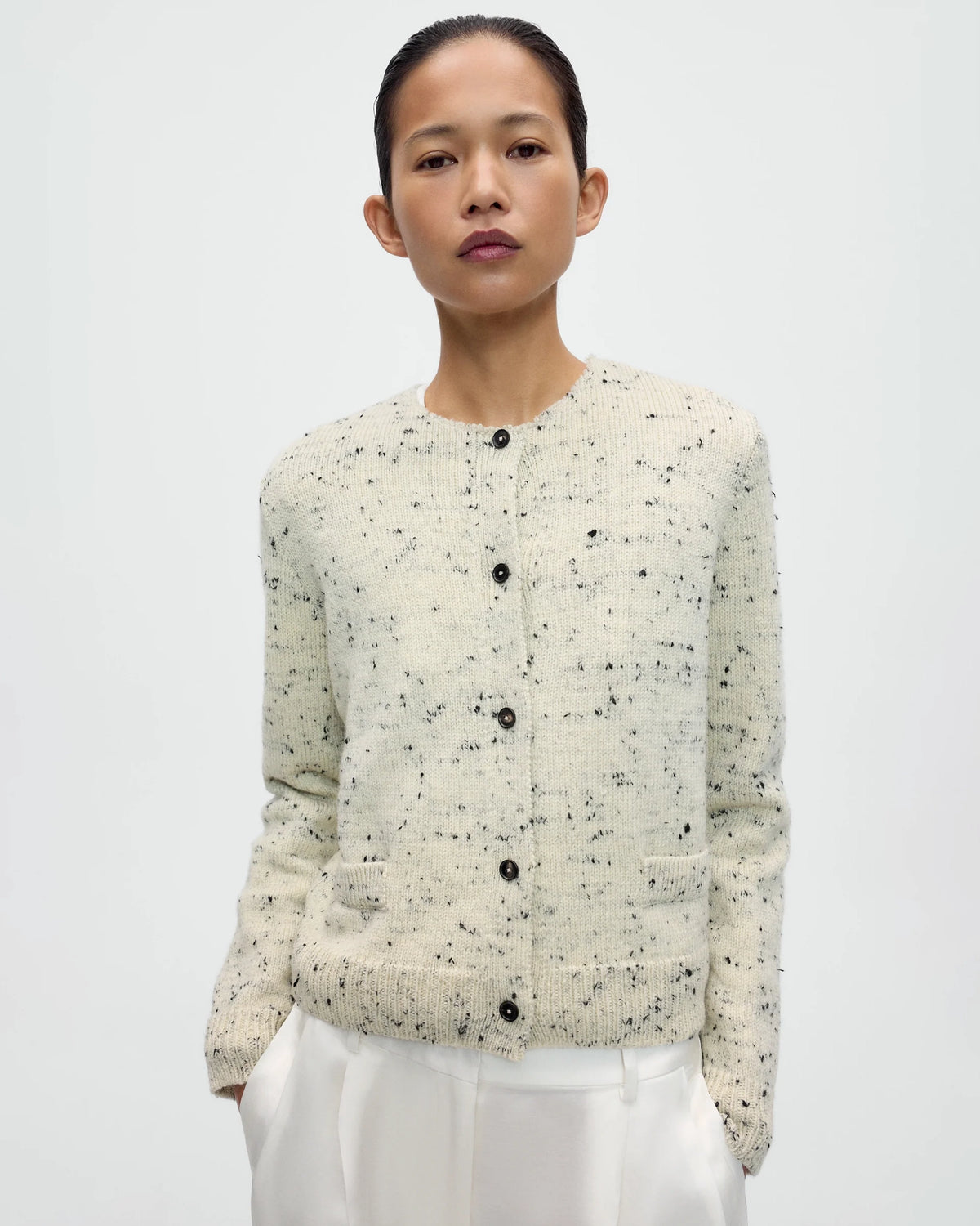 Model wearing CORDERA Merino Wool Flecked Cardigan in natural with a flecked chunky knit, button front and patch pockets.