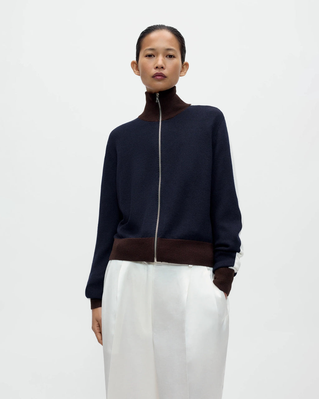 Model wearing CORDERA Merino Wool Sporty Cardigan in navy with white sleeve stripes, brown ribbed trim and a front zip closure.