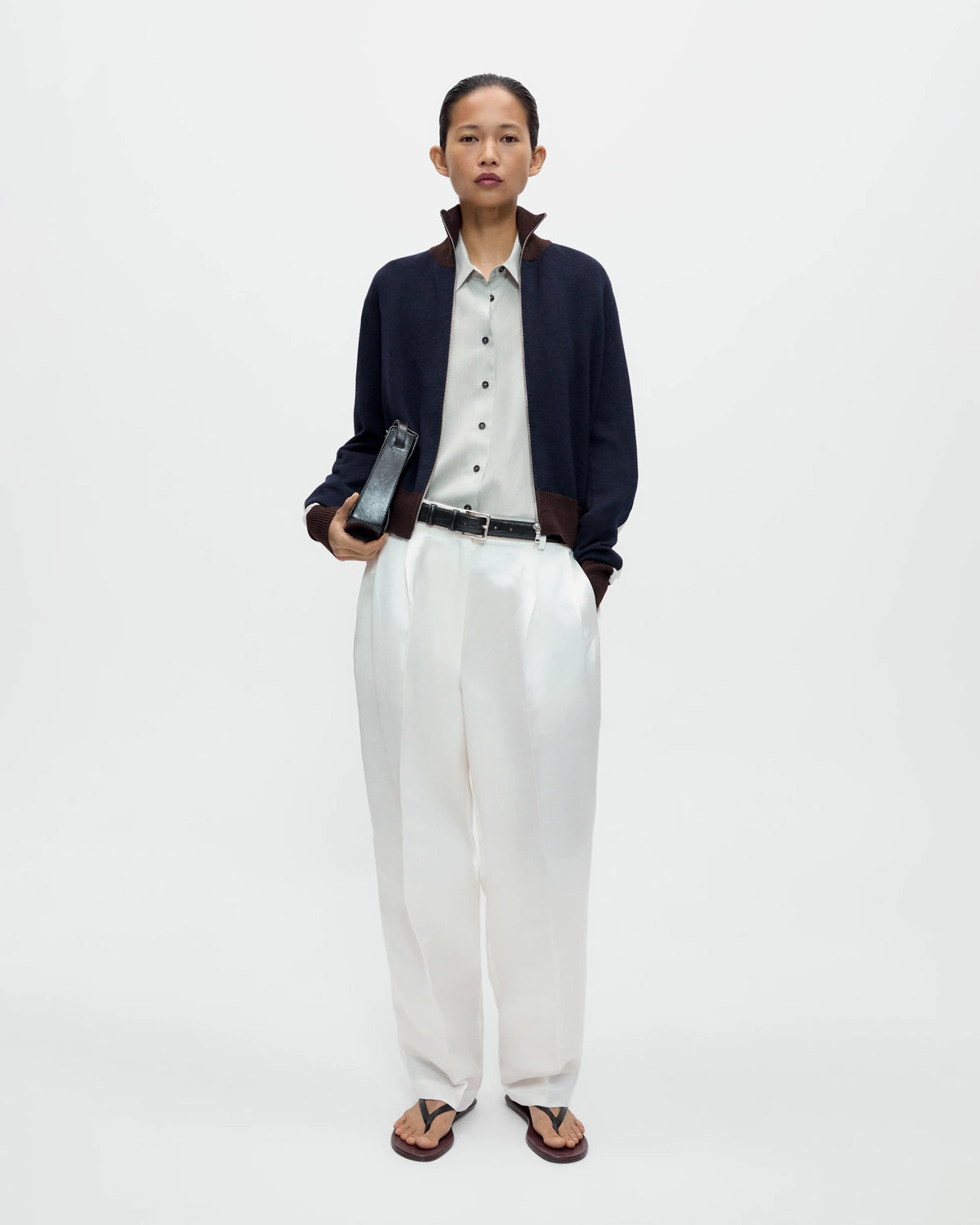 Model wearing CORDERA Merino Wool Sporty Cardigan in navy with white sleeve stripes, brown ribbed trim and a front zip closure.