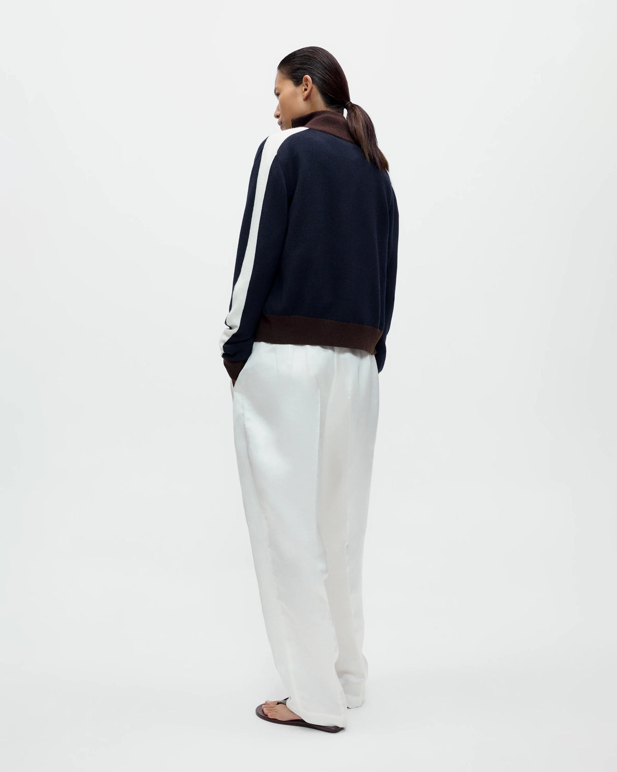 Model wearing CORDERA Merino Wool Sporty Cardigan in navy with white sleeve stripes, brown ribbed trim and a front zip closure.
