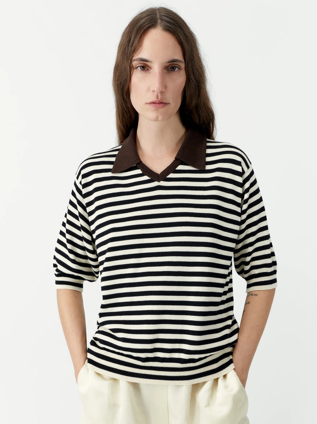 Person wearing a black and white striped shirt with a brown collar on a plain background