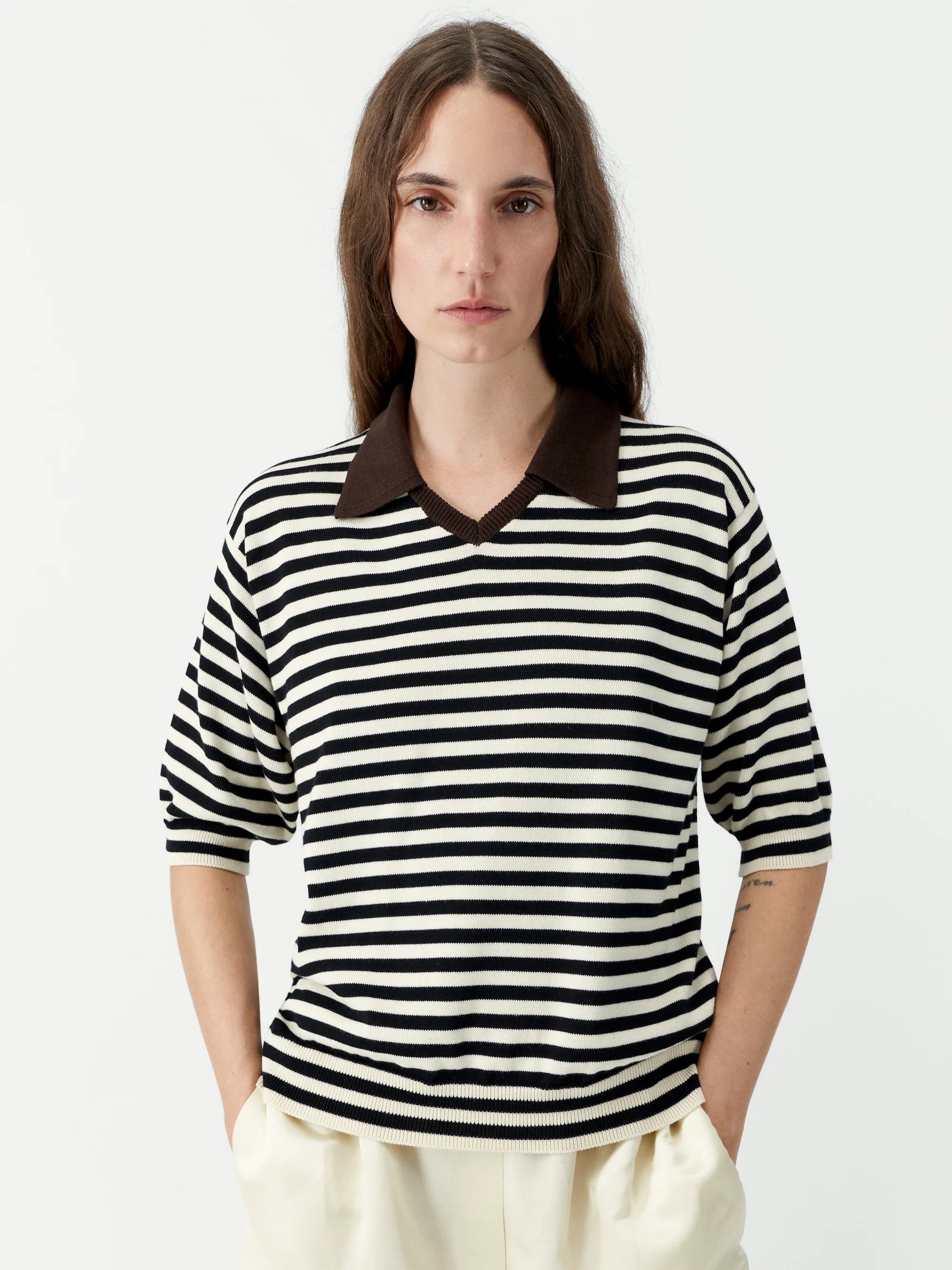 Person wearing a black and white striped shirt with a brown collar on a plain background