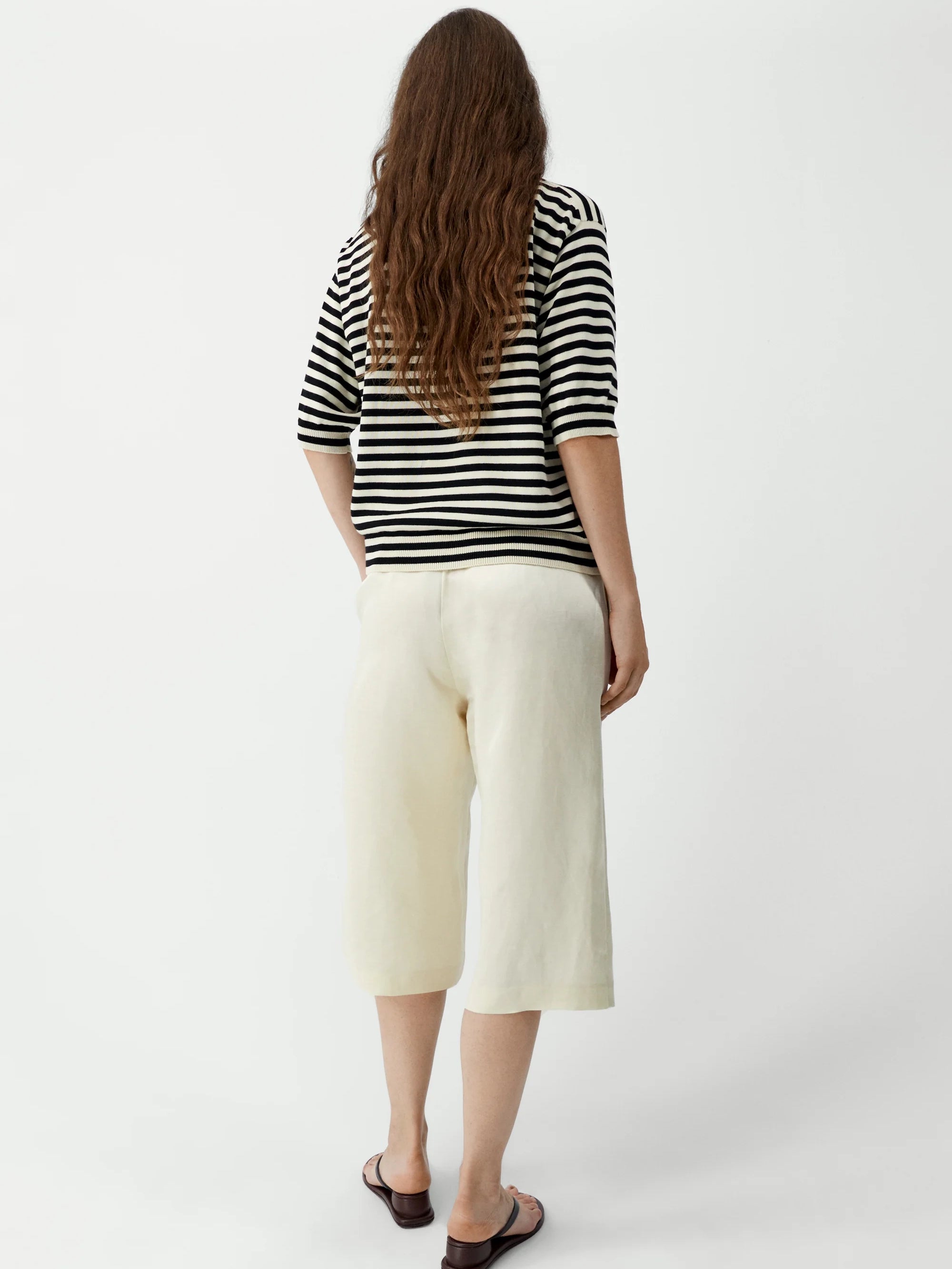 Person wearing a striped shirt and white pants on a plain background