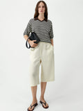 Woman wearing a black and white striped shirt with cream-colored pants on a white background