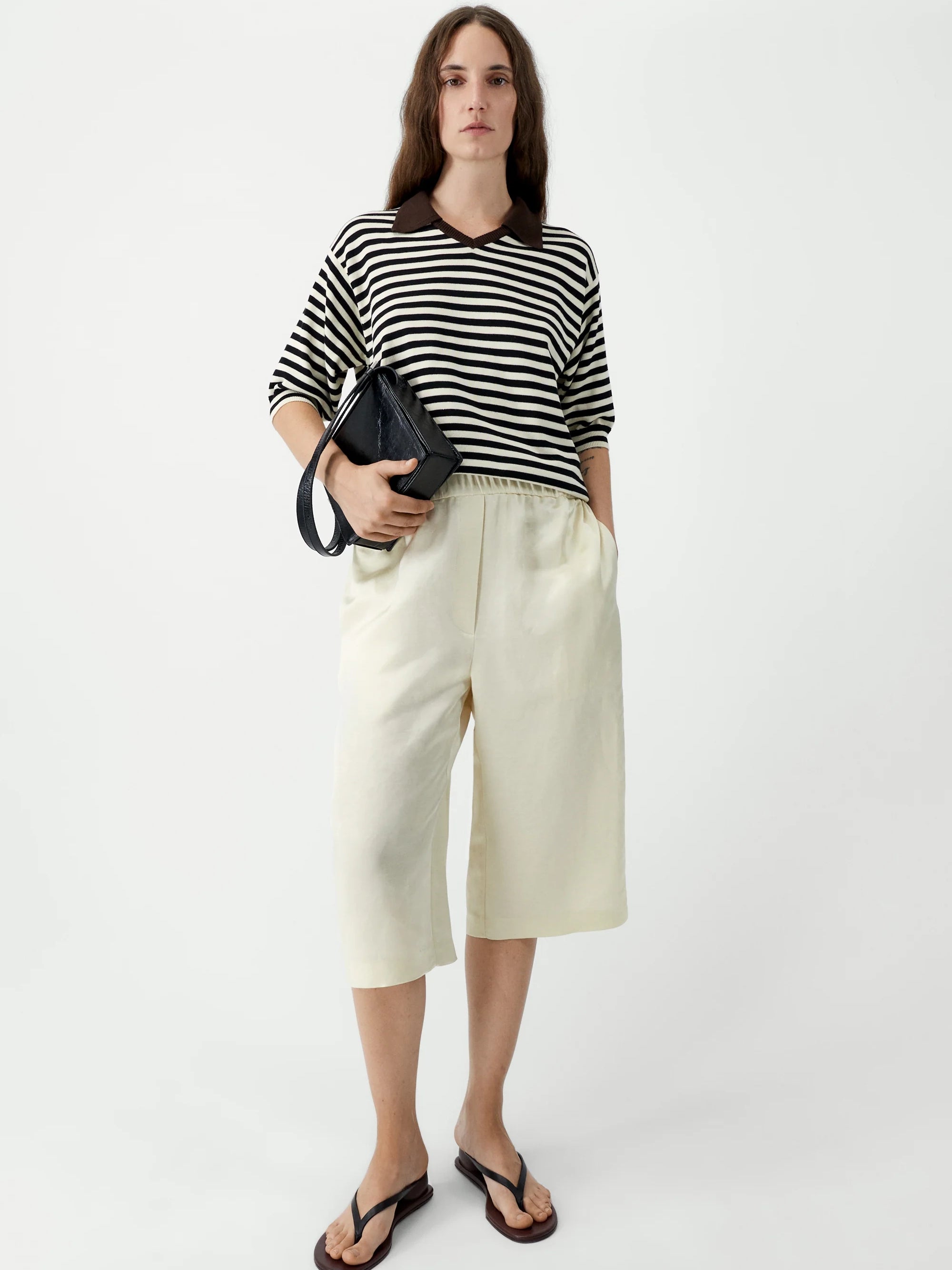 Woman wearing a black and white striped shirt with cream-colored pants on a white background