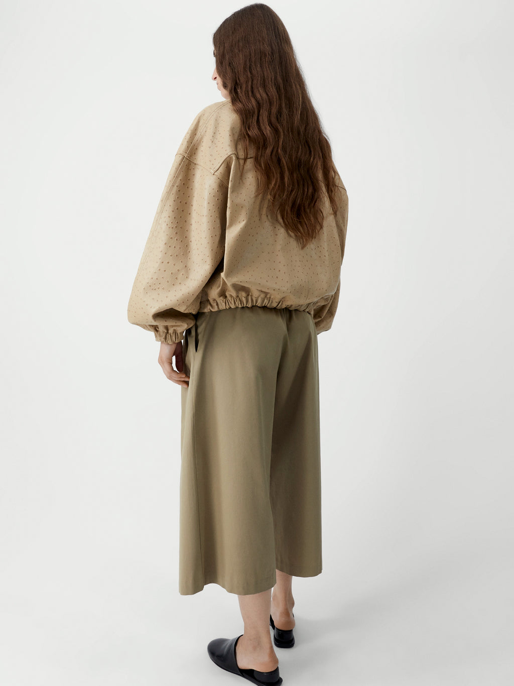 Woman wearing a beige sweater and olive green skirt on a white background