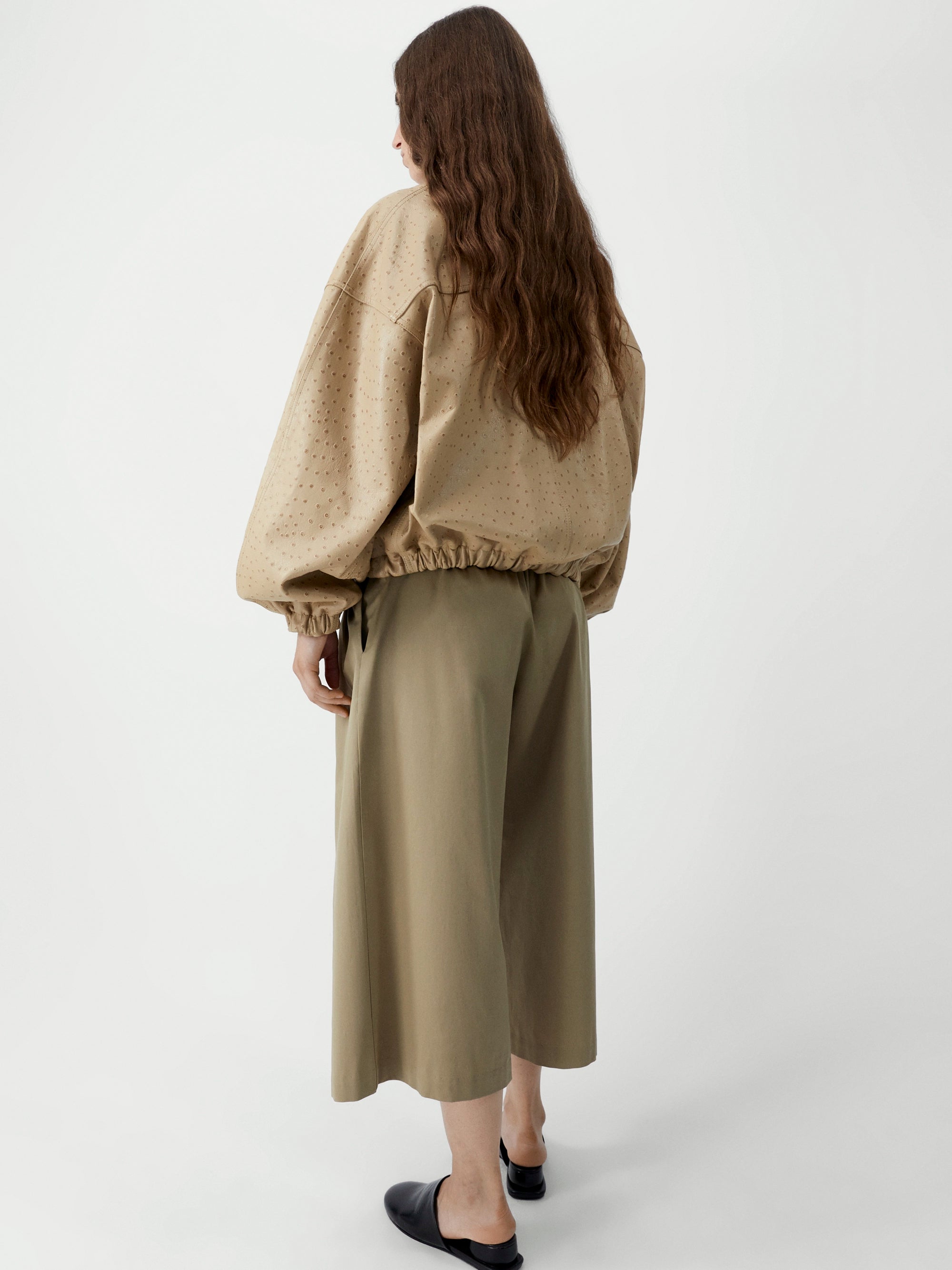 Woman wearing a beige sweater and olive green skirt on a white background