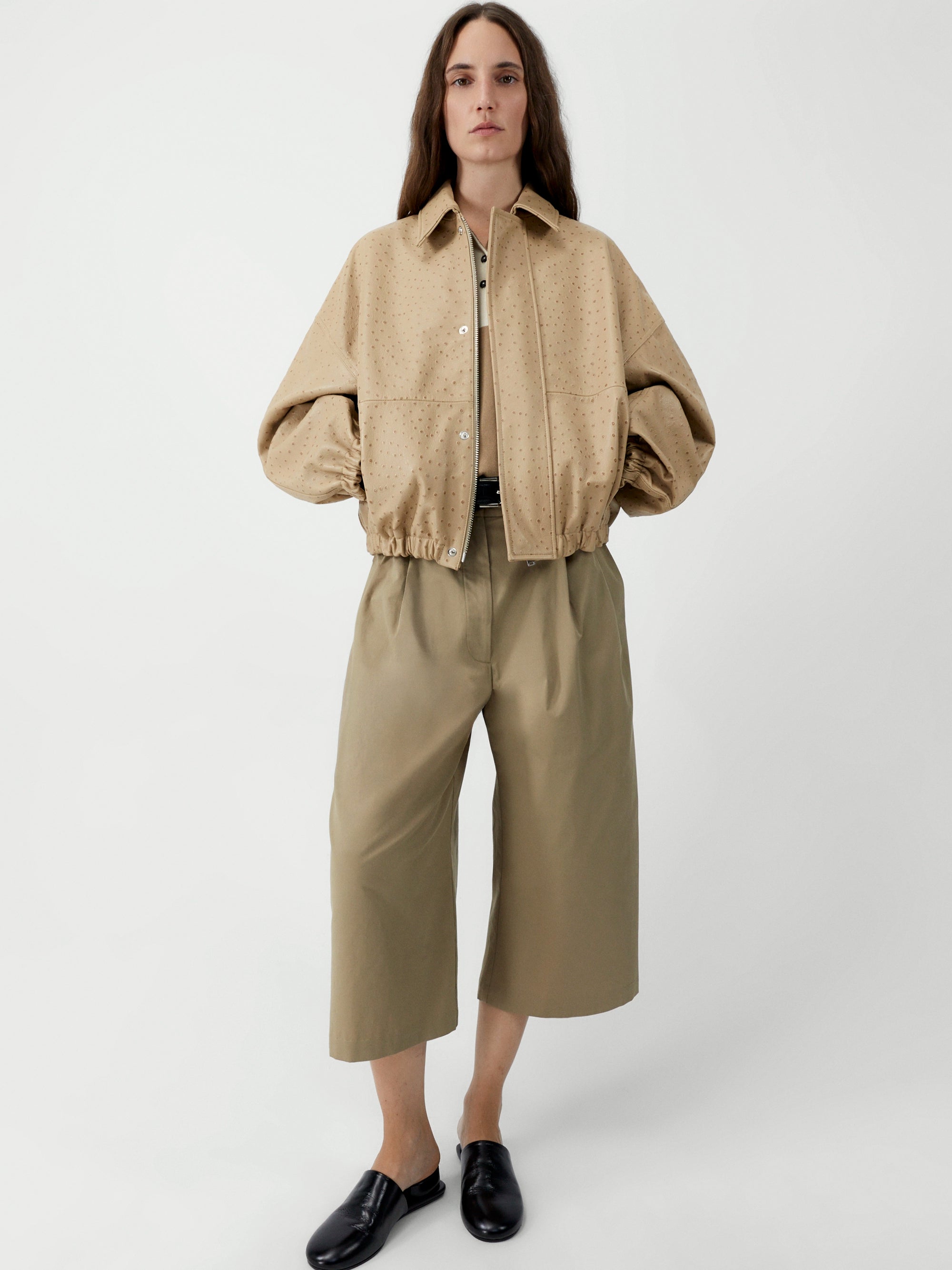 Person wearing a beige jacket and pants on a white background