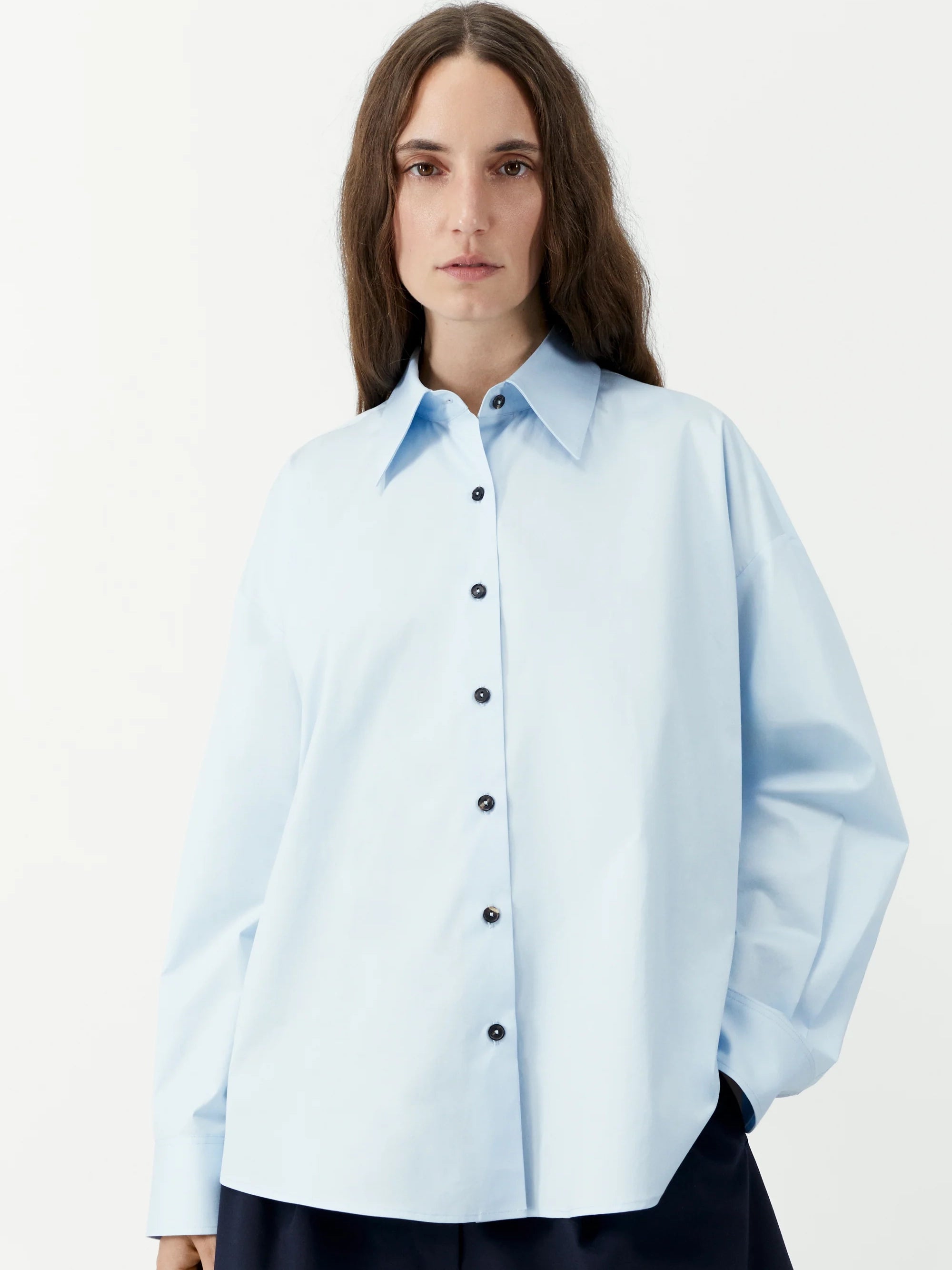 Person wearing a light blue shirt with black buttons on a white background