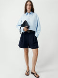 Person wearing a light blue shirt and black shorts holding a black clutch against a white background