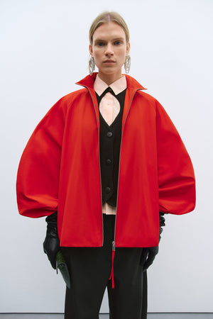 Person wearing a bright red coat over a black outfit on a white background