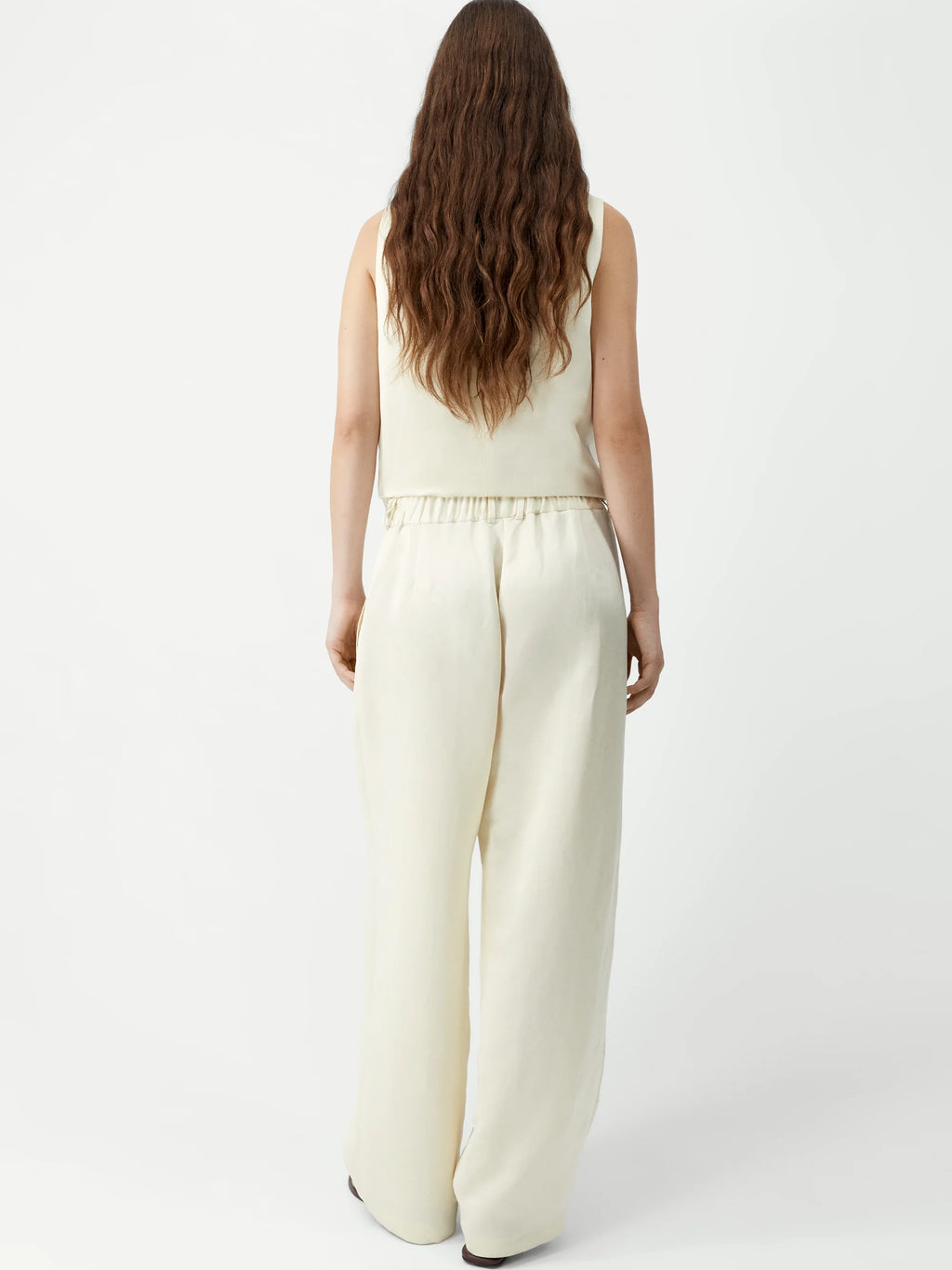 Woman wearing a cream sleeveless top and wide-leg pants on a white background