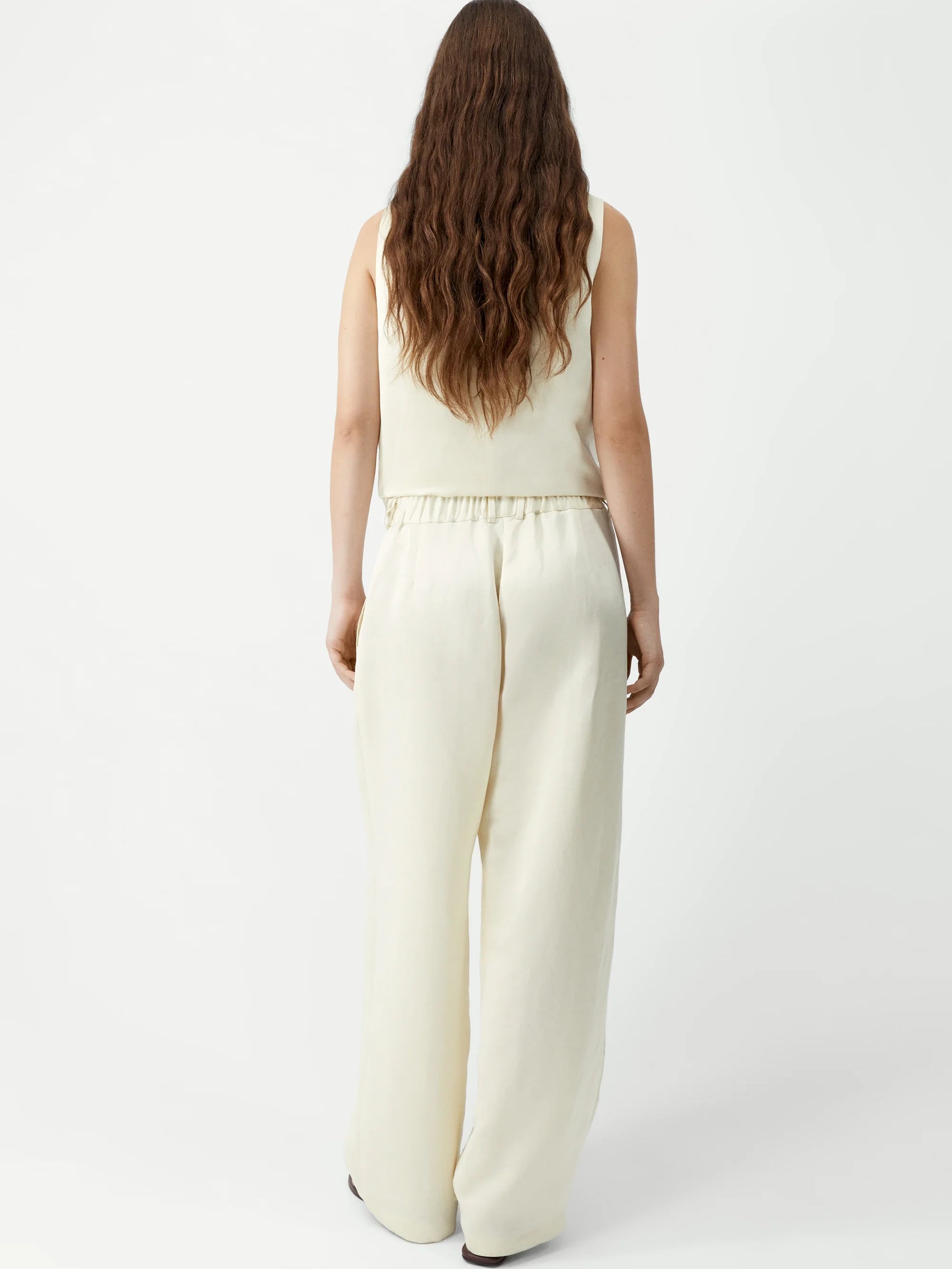 Woman wearing a cream sleeveless top and wide-leg pants on a white background