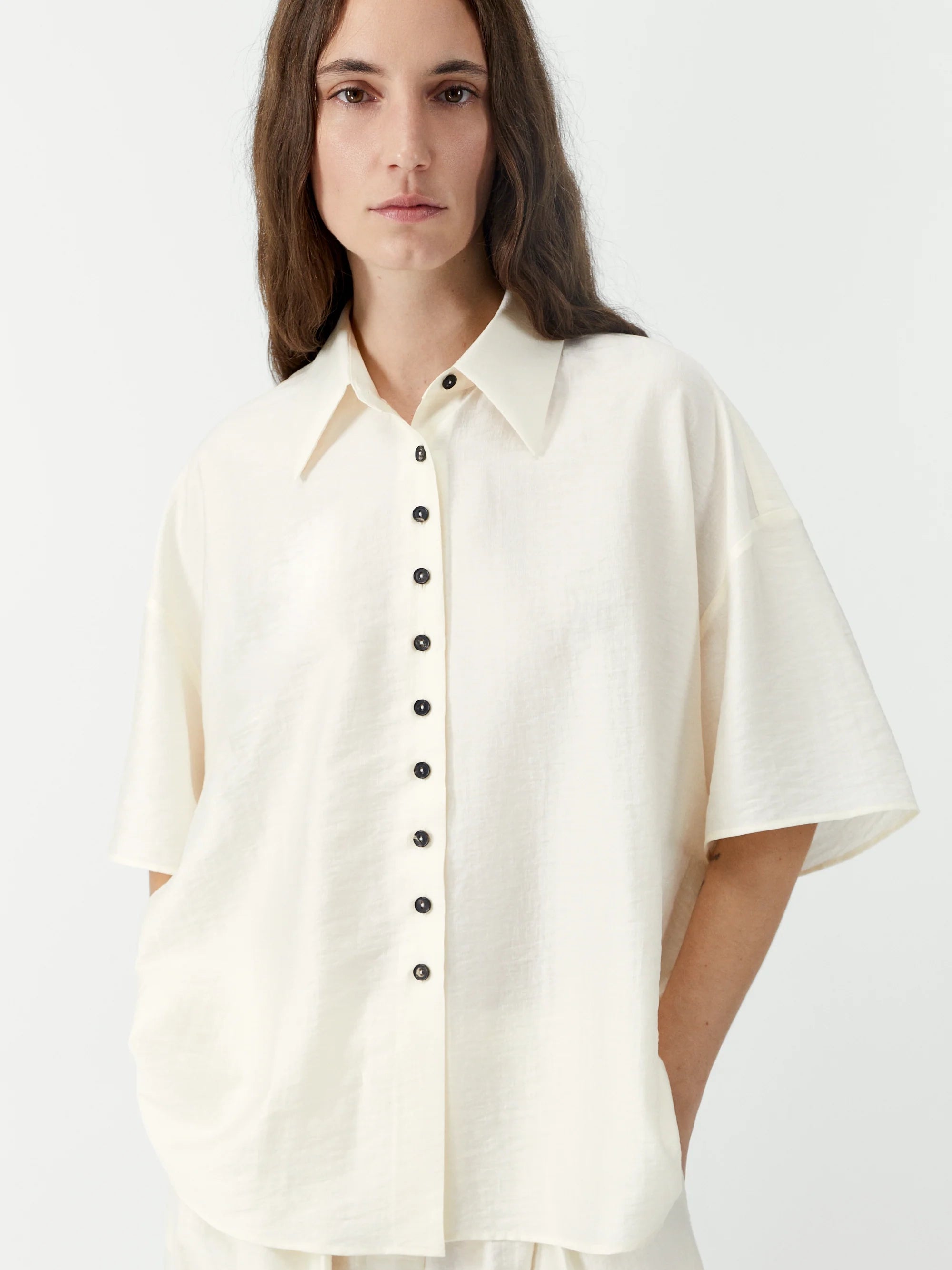 Woman wearing a white button-up shirt with black buttons on a light gray background