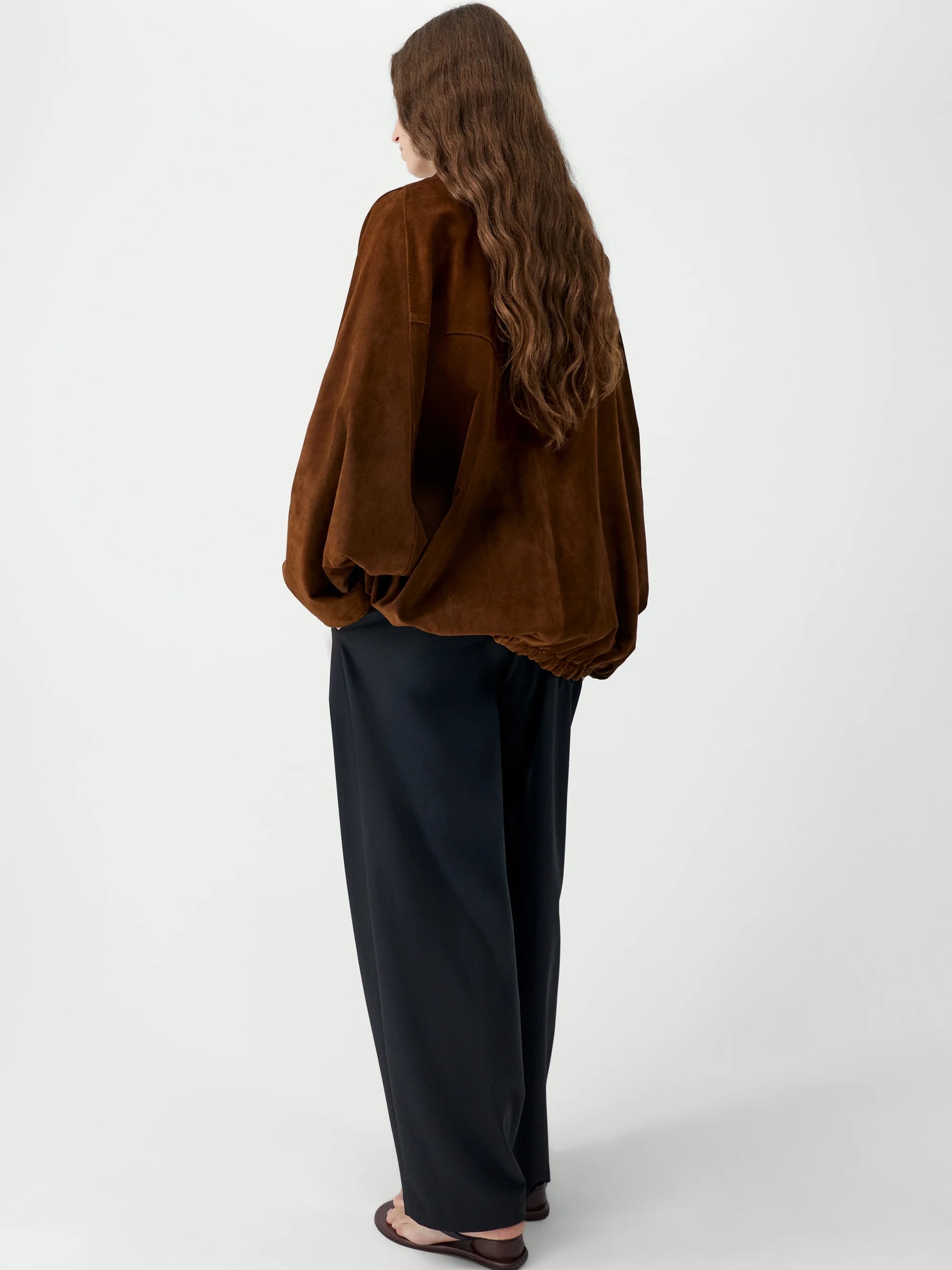 Person wearing a brown sweater and black pants on a white background