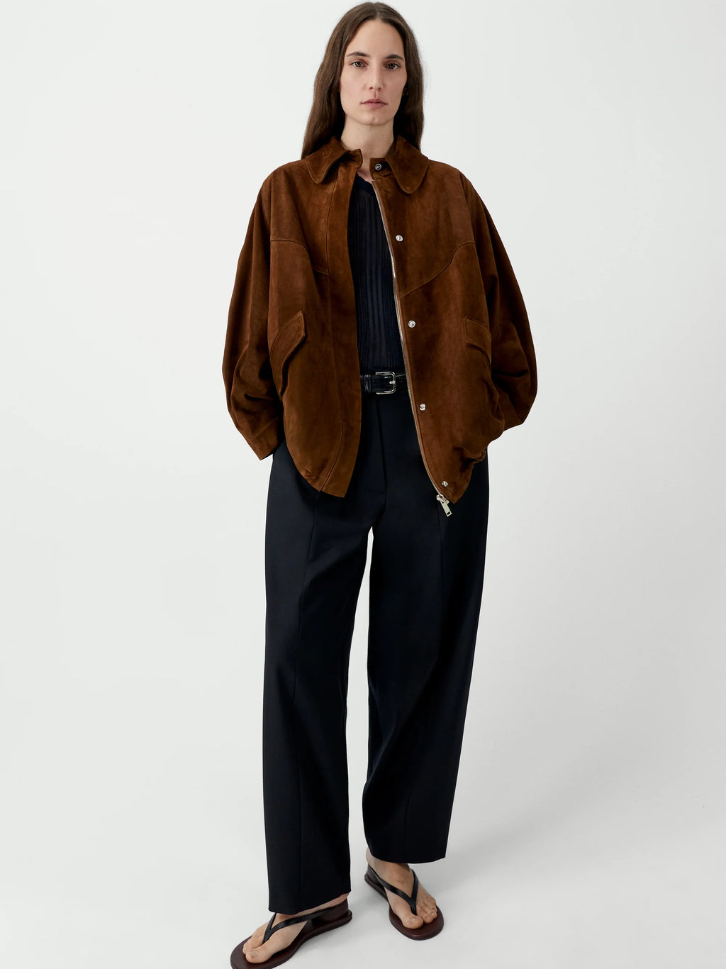 Person wearing a brown jacket and black pants on a white background