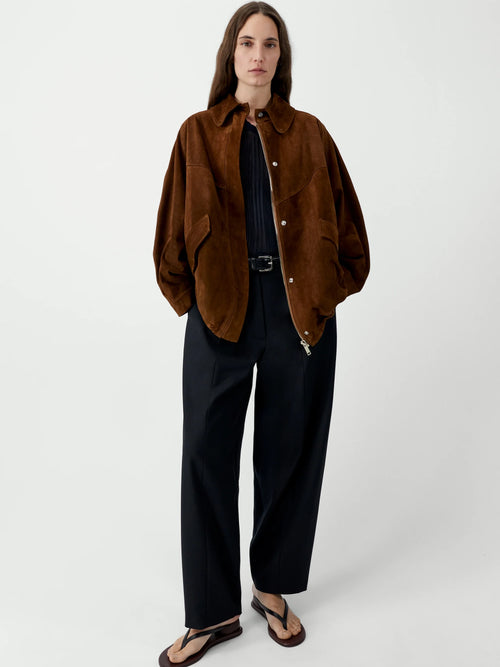 Person wearing a brown jacket and black pants on a white background