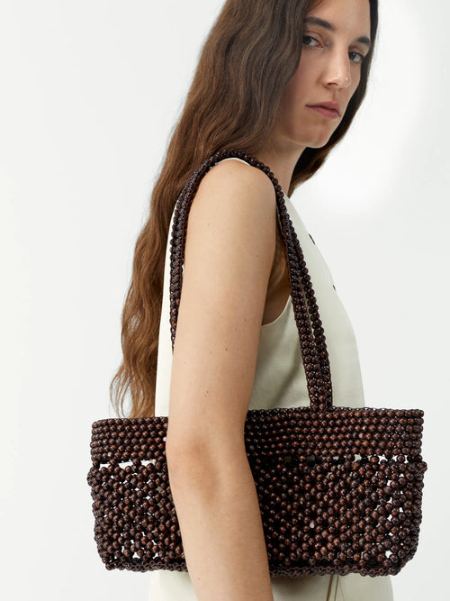 Woman holding a brown beaded handbag against a white background