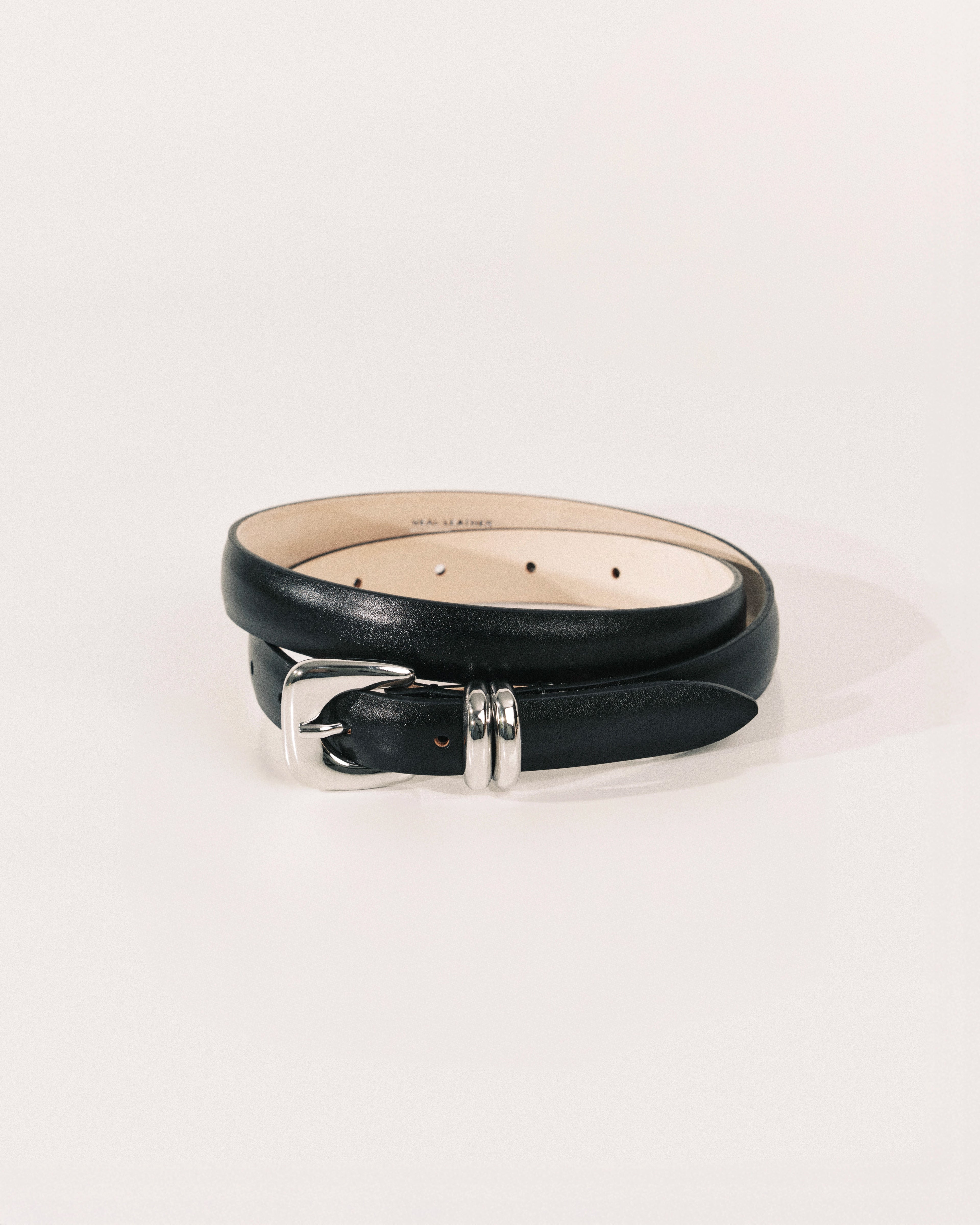 Black leather belt by Déhanche with sculptural silver-tone buckle and curved metal keeper.