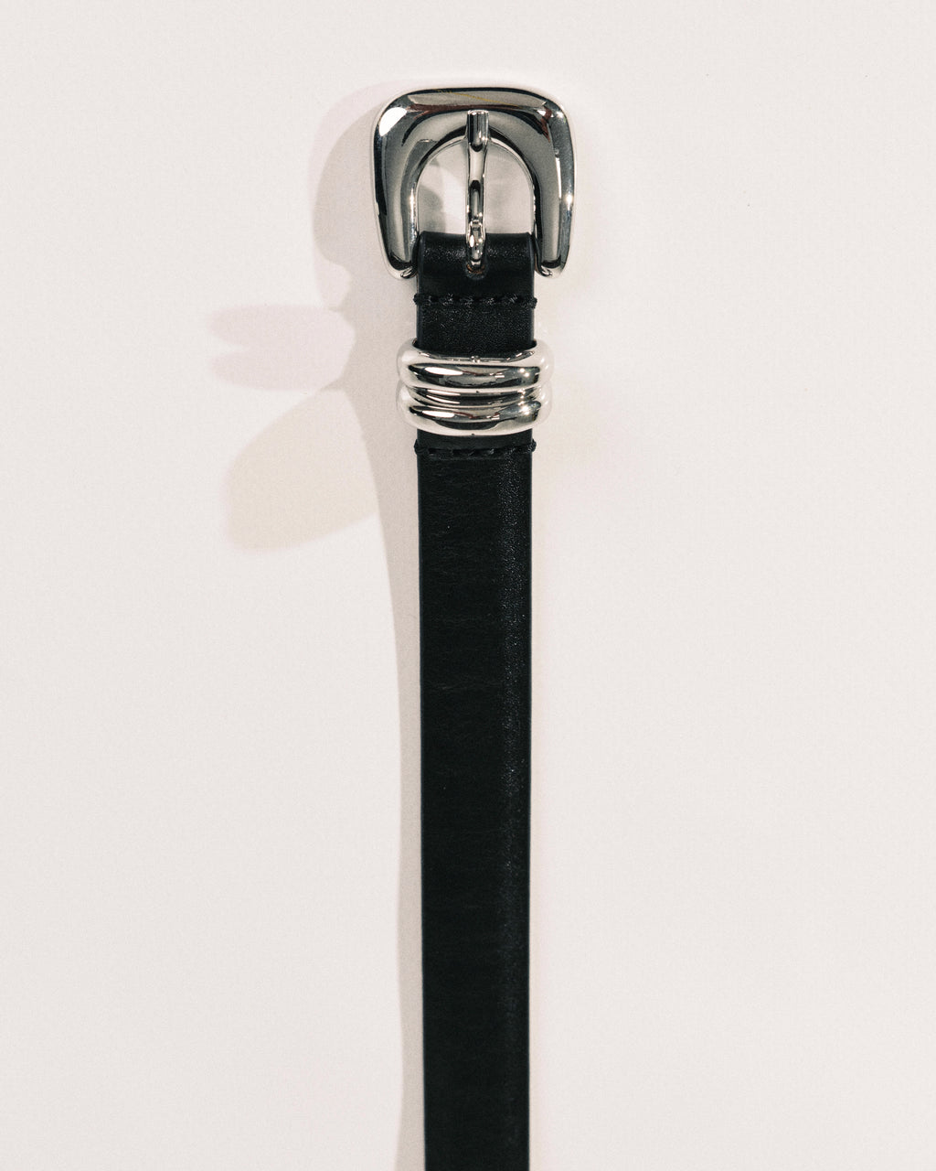 Black leather belt by Déhanche with sculptural silver-tone buckle and curved metal keeper.