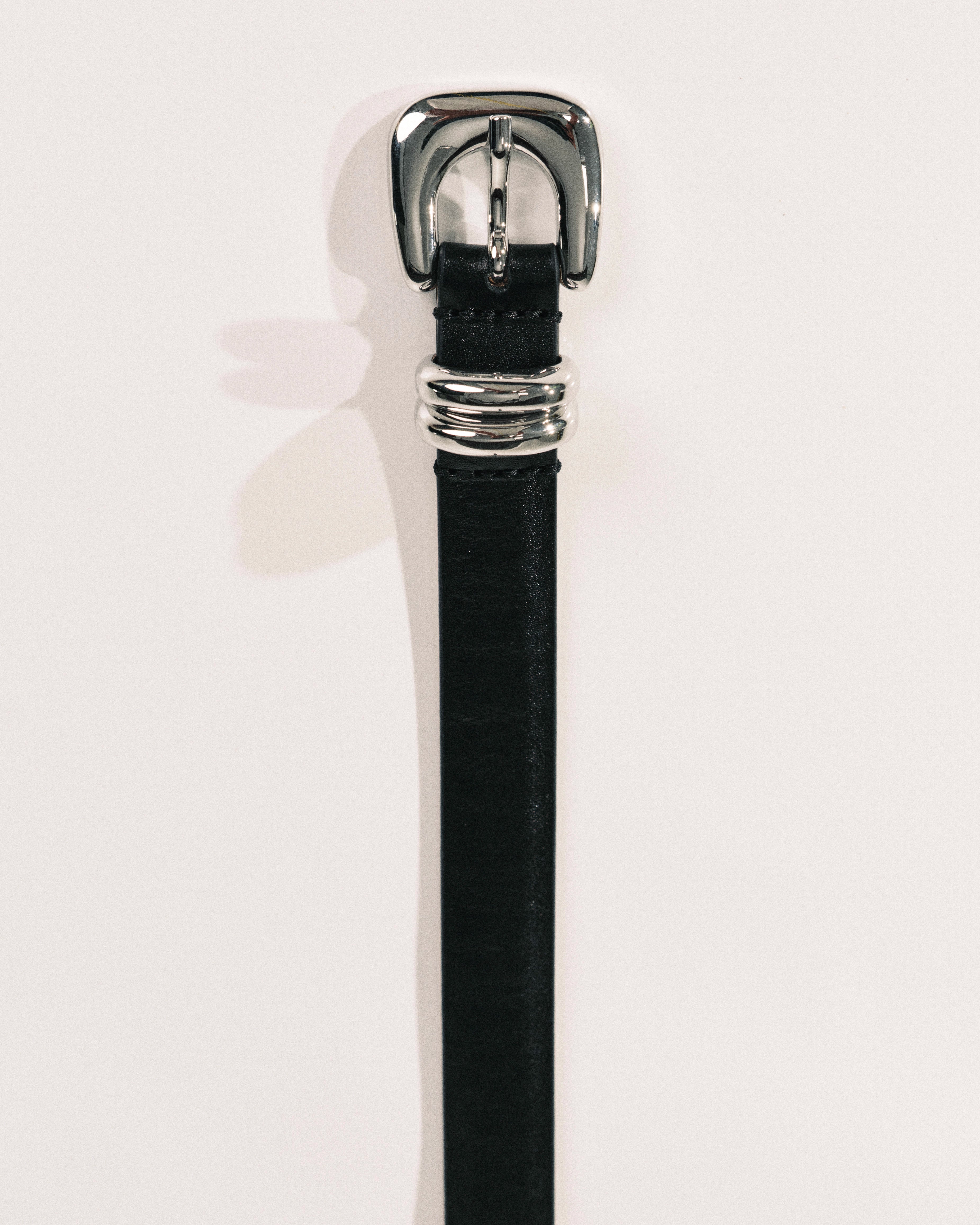 Black leather belt by Déhanche with sculptural silver-tone buckle and curved metal keeper.