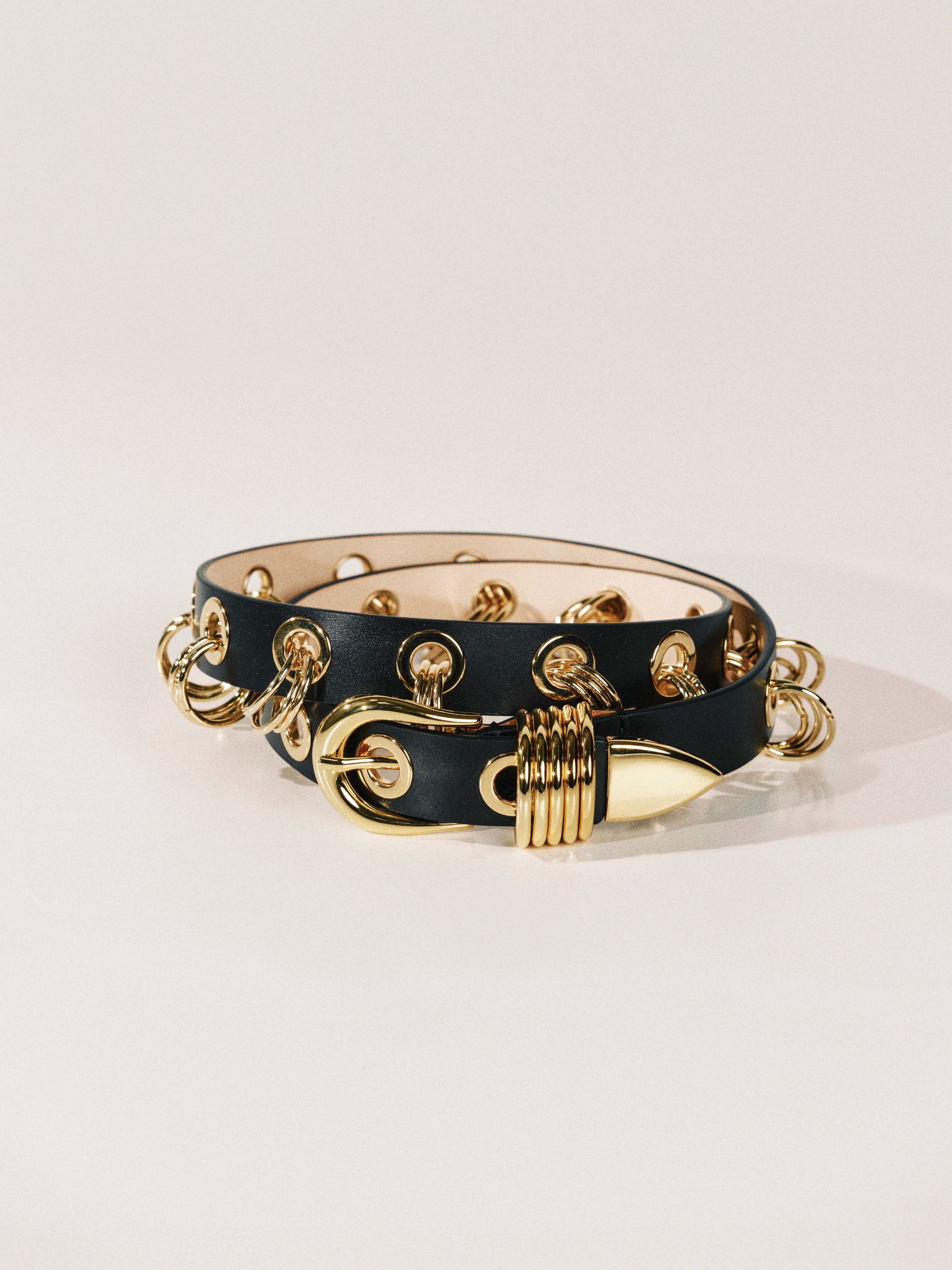 Black leather bracelet with gold chain and clasp on a light gray background