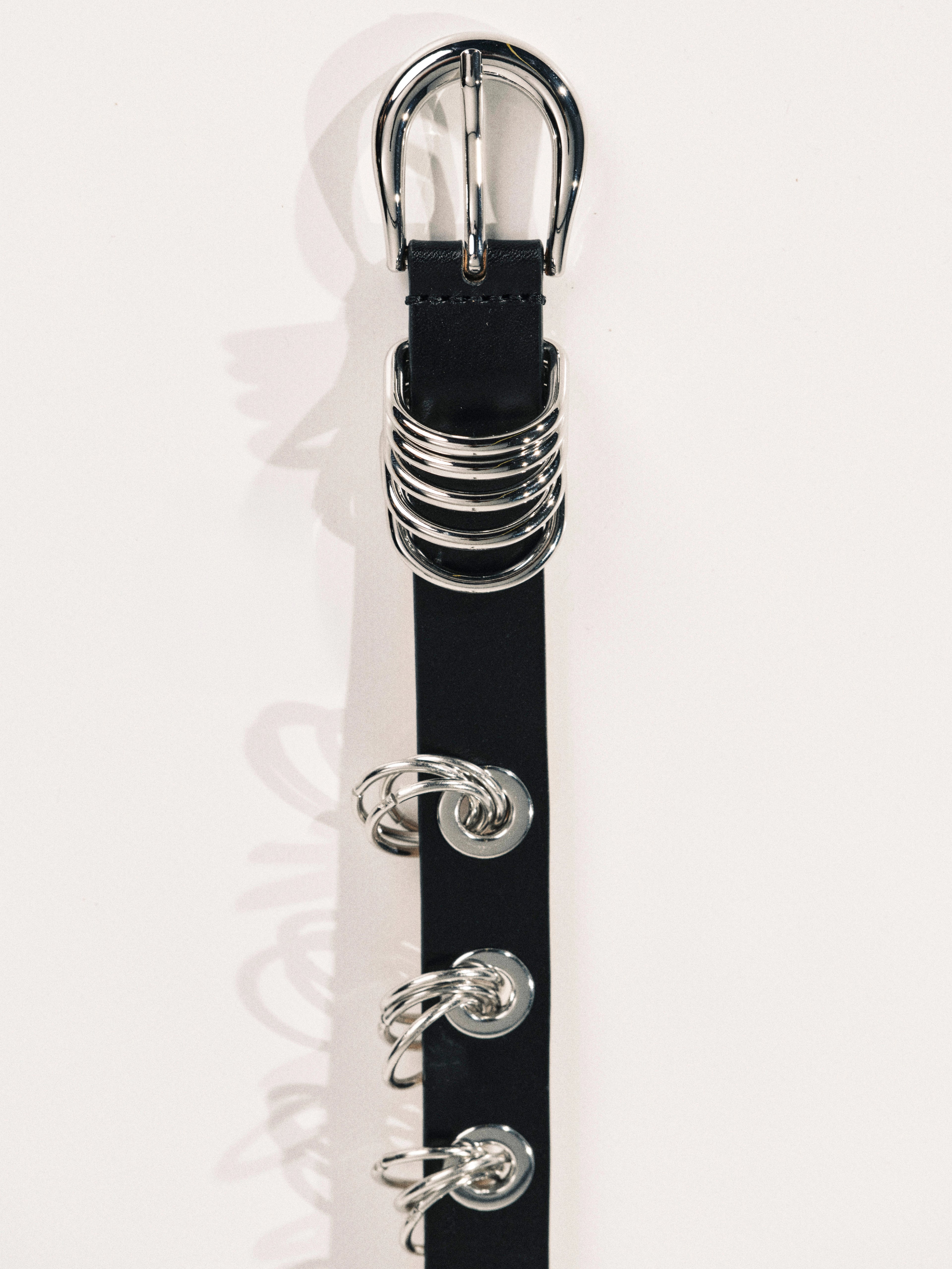 Black belt with silver buckle and decorative rings on a white background
