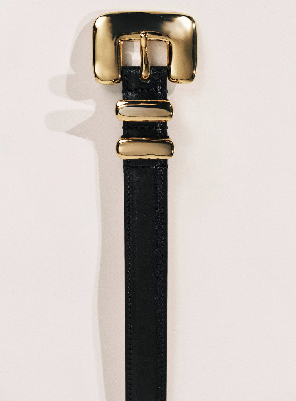 Black belt with a gold buckle on a light pink background