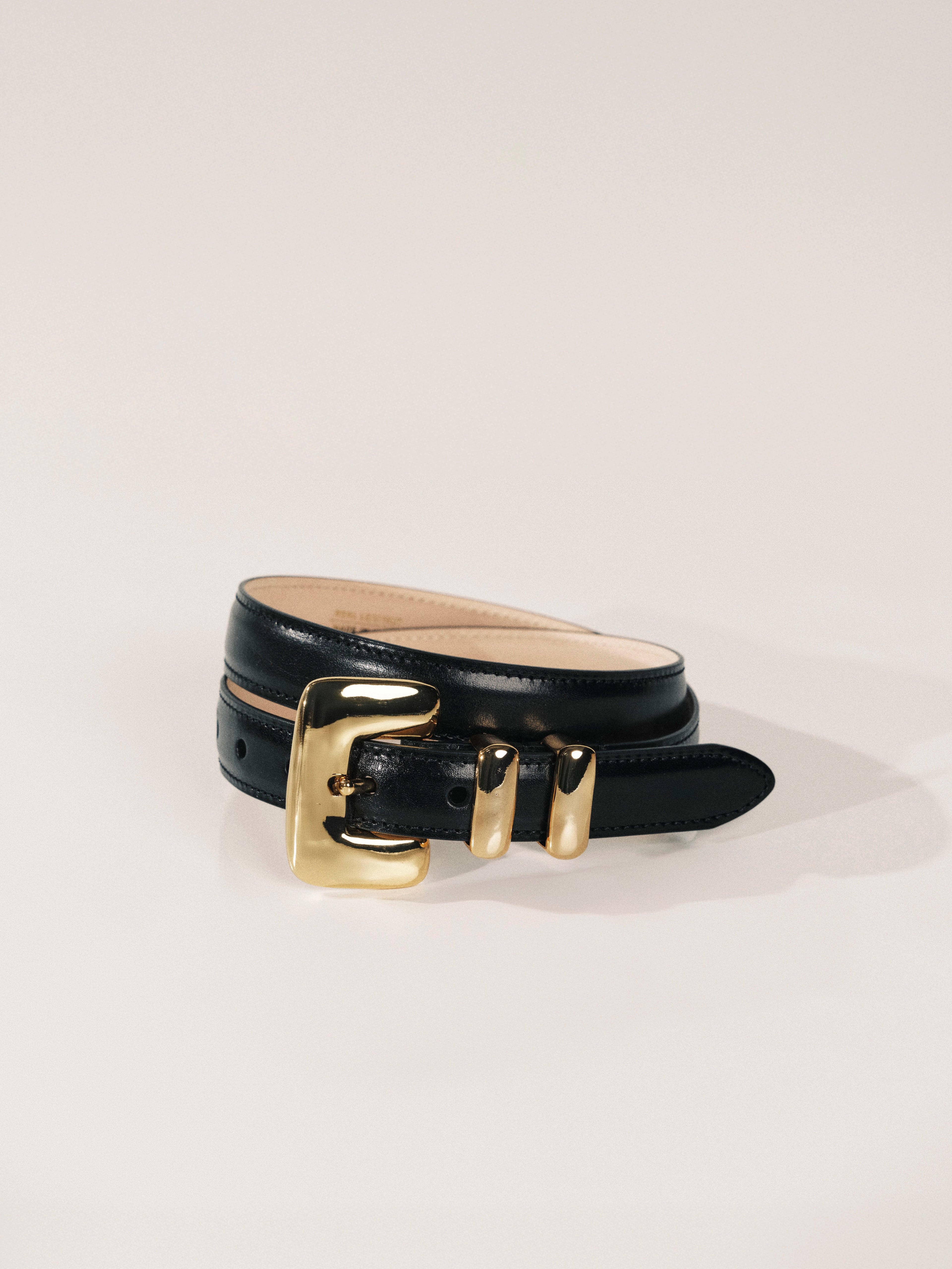 Black leather belt with a gold buckle on a light gray background