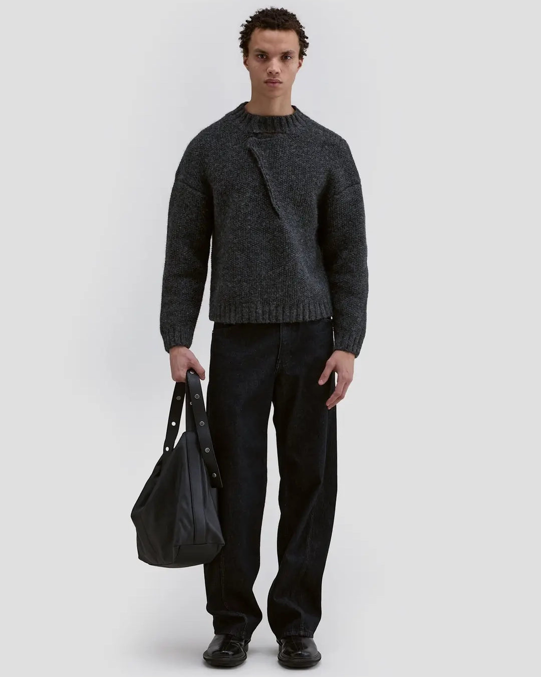 ￼Model wearing Eckhaus Latta Bend Jean in black rinse with a loose bowed leg and twisted side seams.