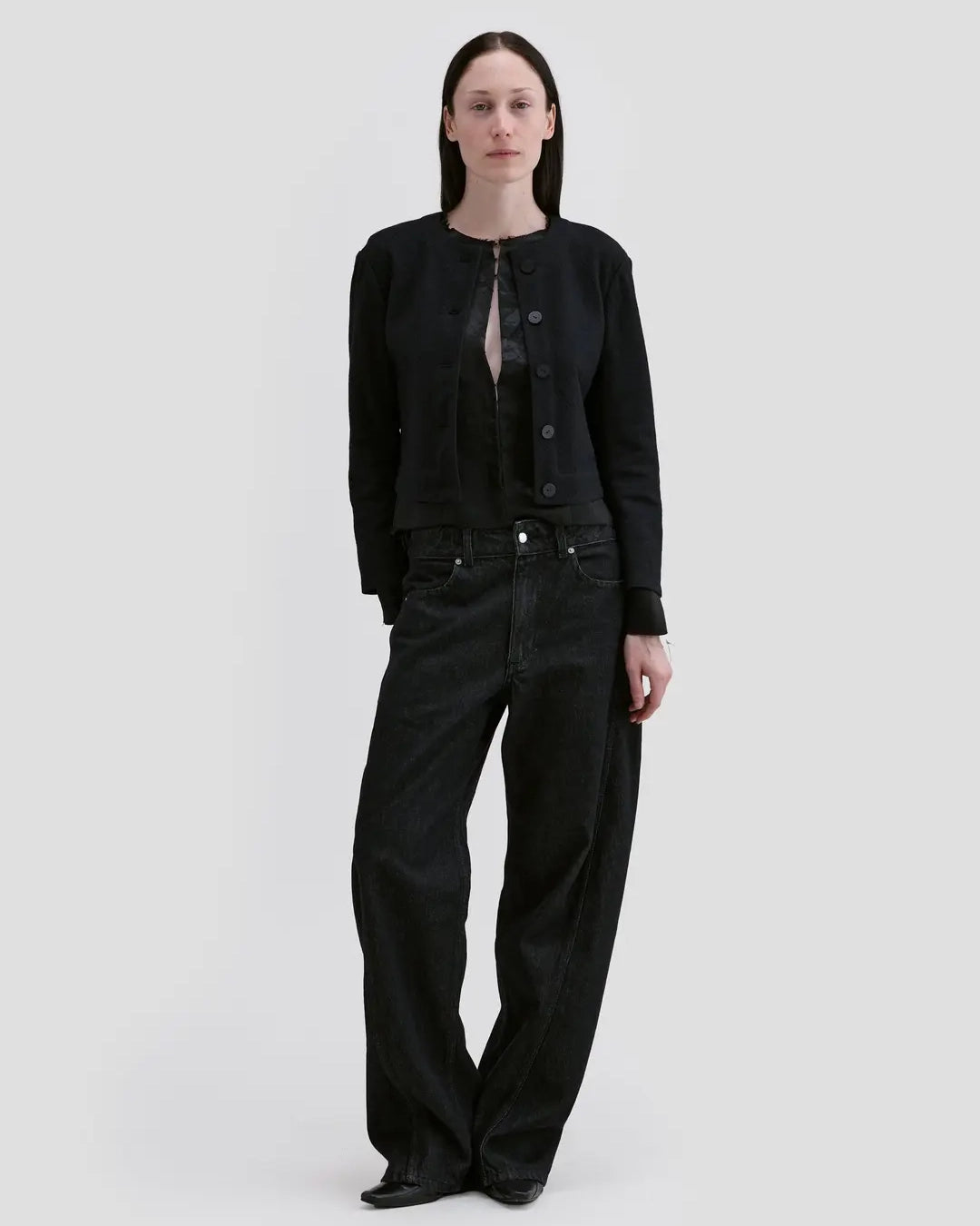 ￼Model wearing Eckhaus Latta Bend Jean in black rinse with a loose bowed leg and twisted side seams.