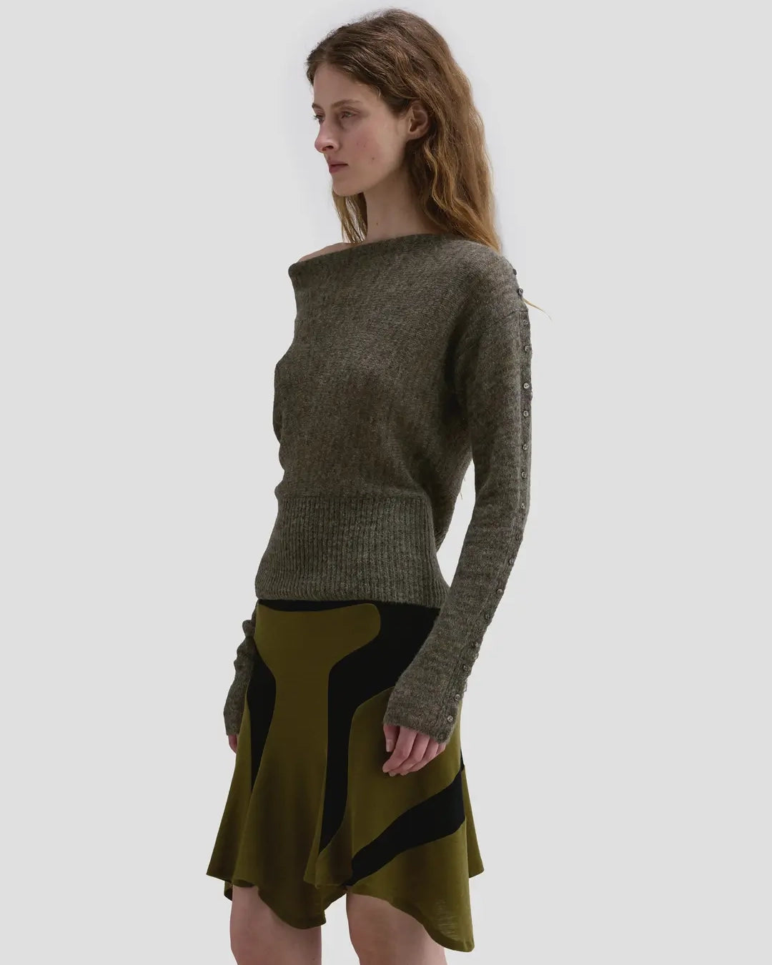 Side view of model wearing the Eckhaus Latta Grid Sweater in fern with a cowl neckline and buttoned sleeves.