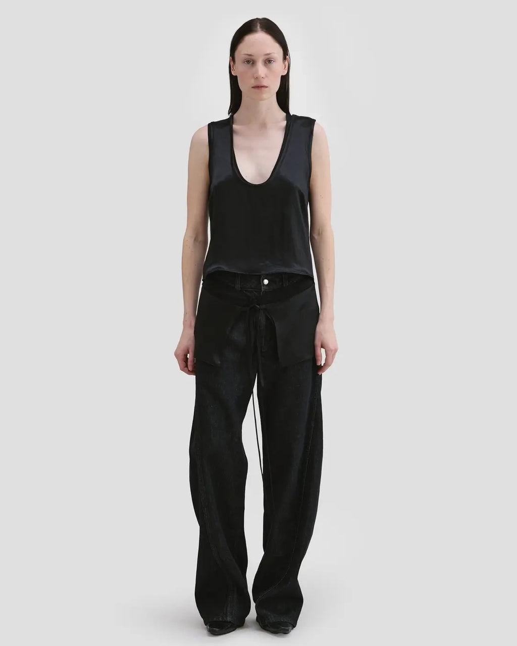 Model wearing Eckhaus Latta Zephyr Tank in oil with a low neckline and front waist peplum.