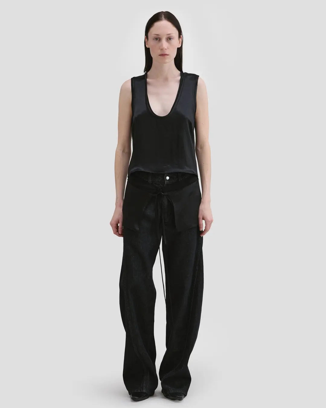 Model wearing Eckhaus Latta Zephyr Tank in oil with a low neckline and front waist peplum.