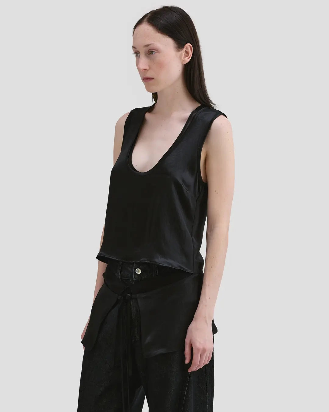 Model wearing Eckhaus Latta Zephyr Tank in oil with a low neckline and front waist peplum.