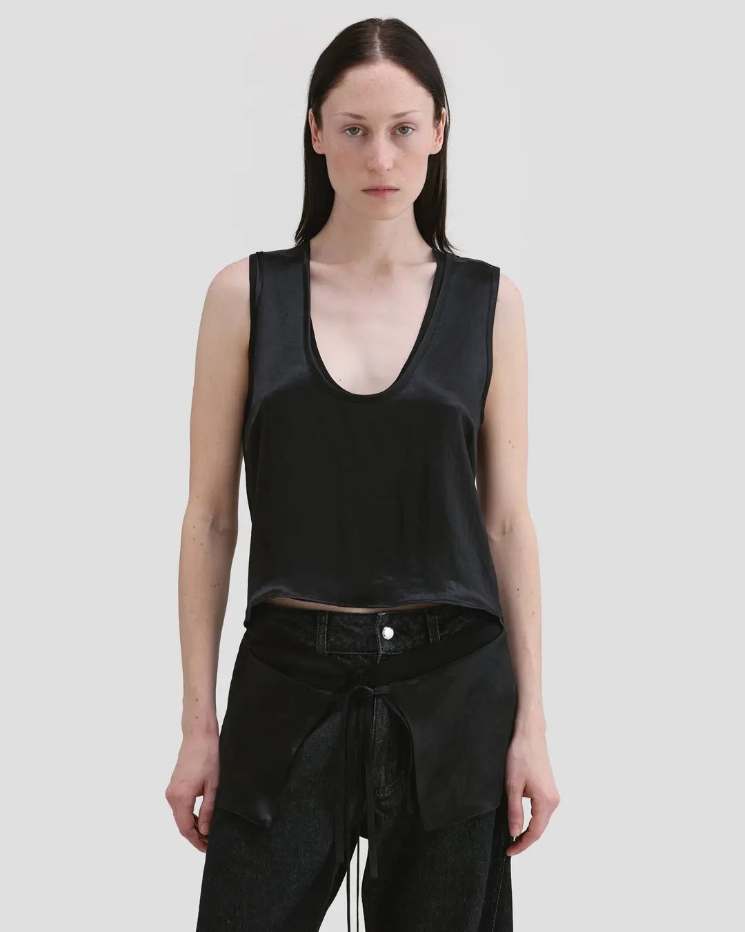 ￼￼Model wearing Eckhaus Latta Zephyr Tank in oil with a low neckline and front waist peplum.