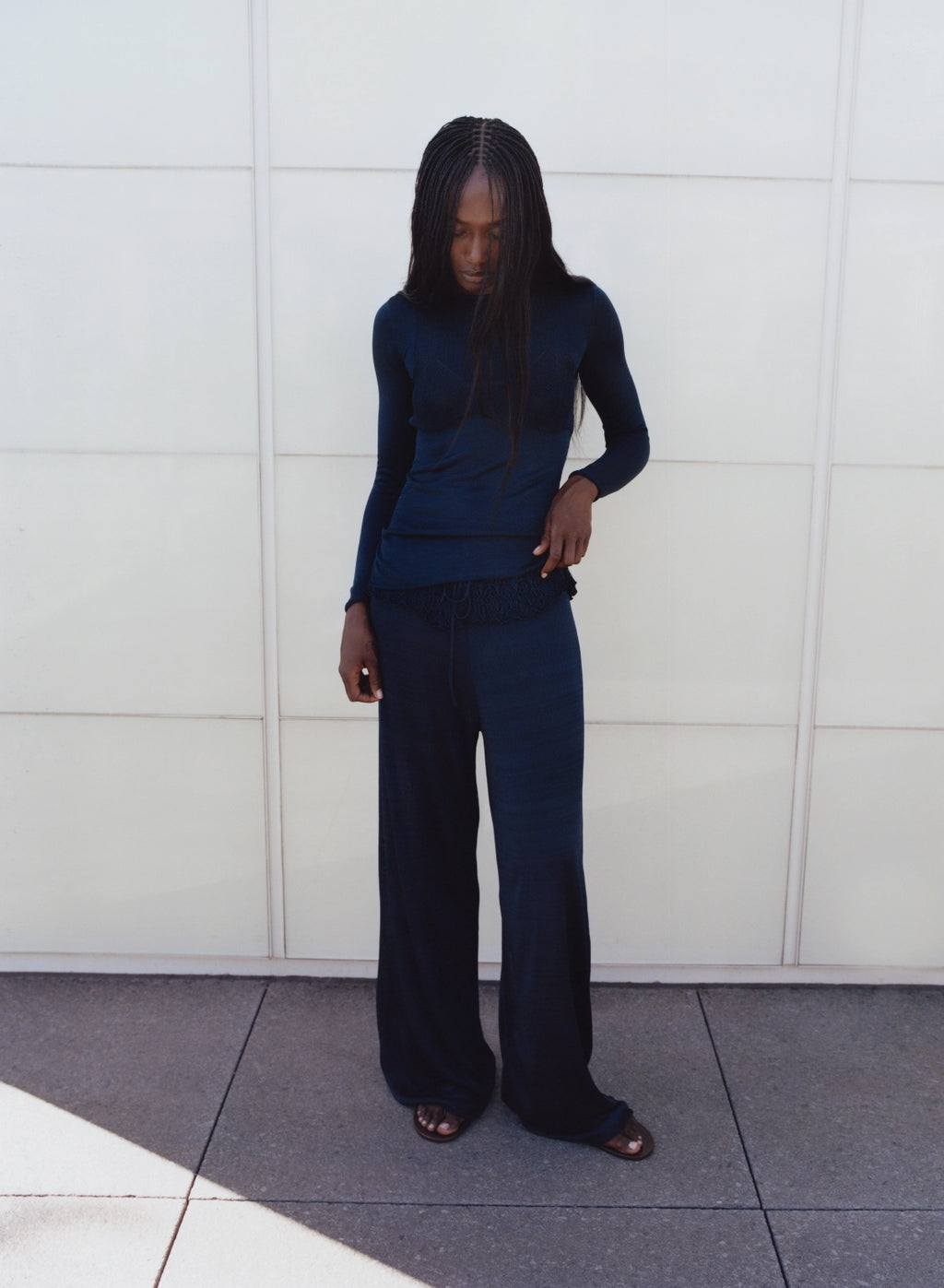 Person wearing a dark blue outfit standing against a white wall.