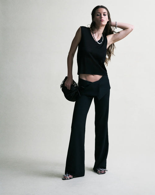 Woman wearing a black sleeveless top and black pants against a white background