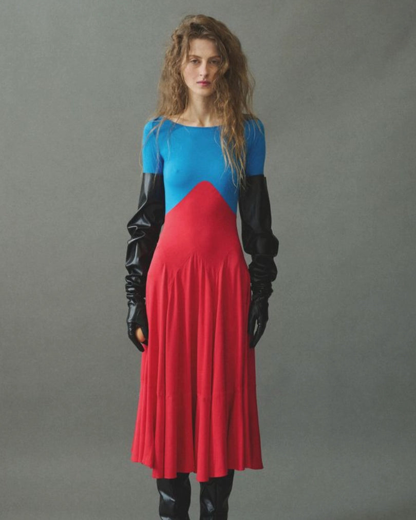 Model wearing red and blue color-block midi dress by EMILY DAWN LONG with a boat neckline, bracelet-length sleeves and full gathered skirt.